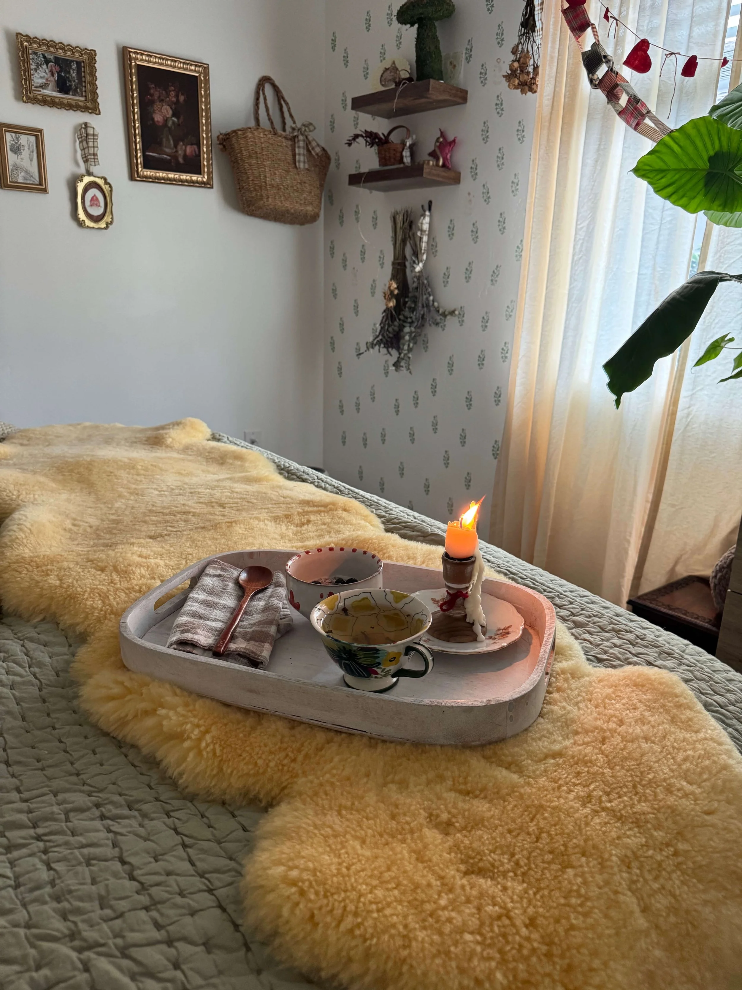 teacup on breakfast tray on bed with candle and bowl of chia pudding on sheepskin rug on bed