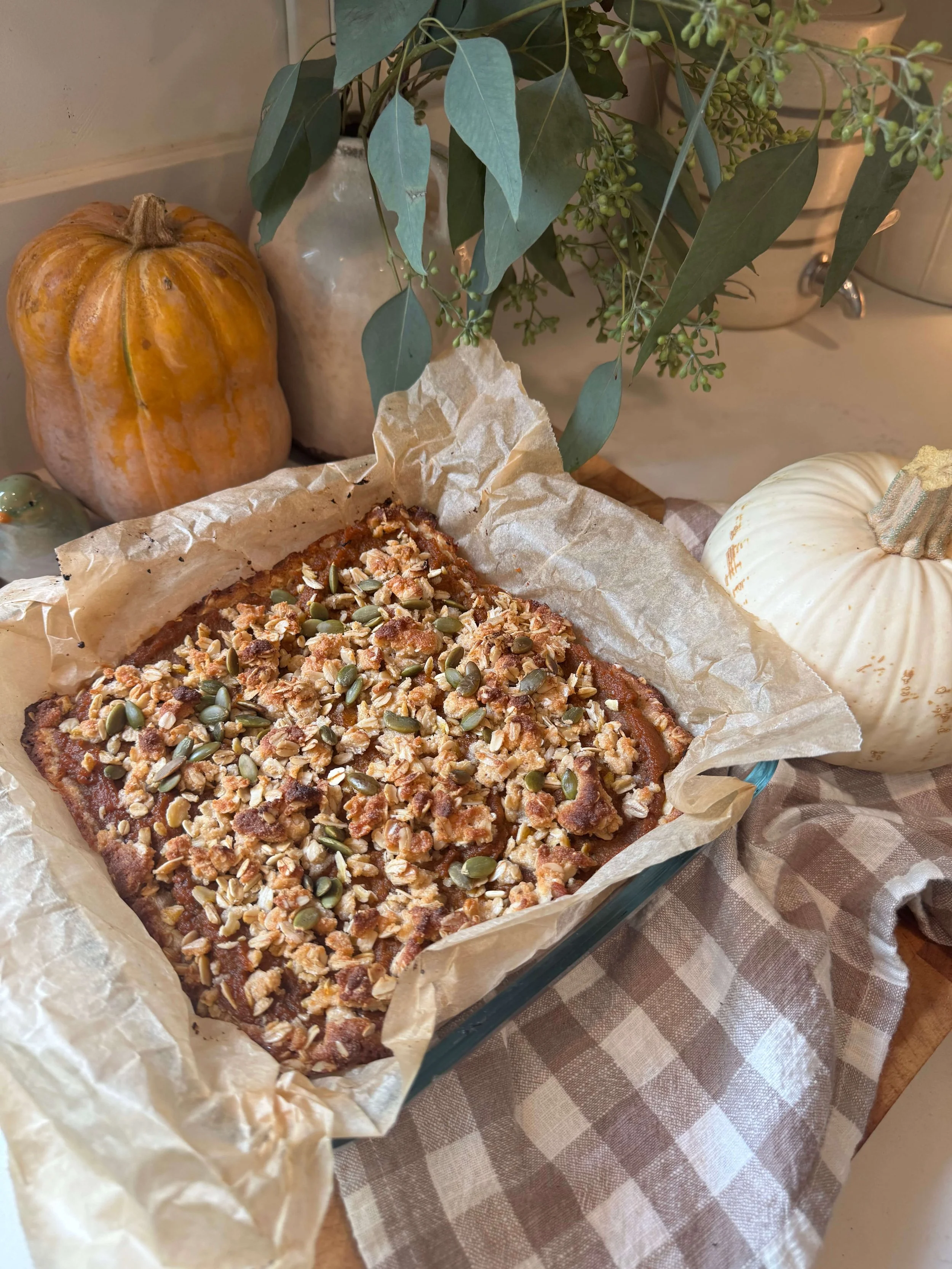 pumpkin pie bars in glass baking pan parchment paper pumpkin on kitchen counter