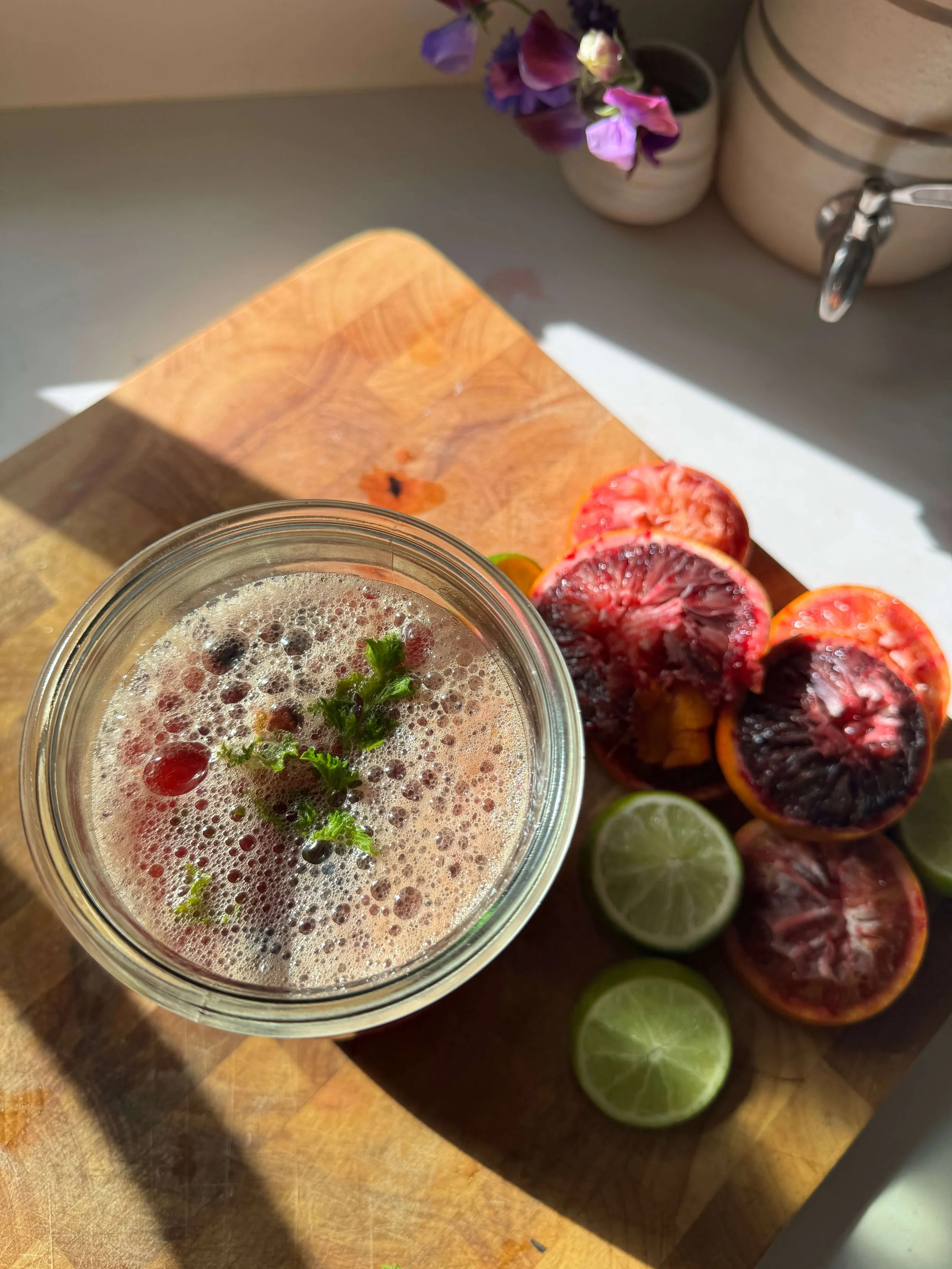 salty lime berry drink in glass with lime and lemon blood orange peeled on kitchen cutting board