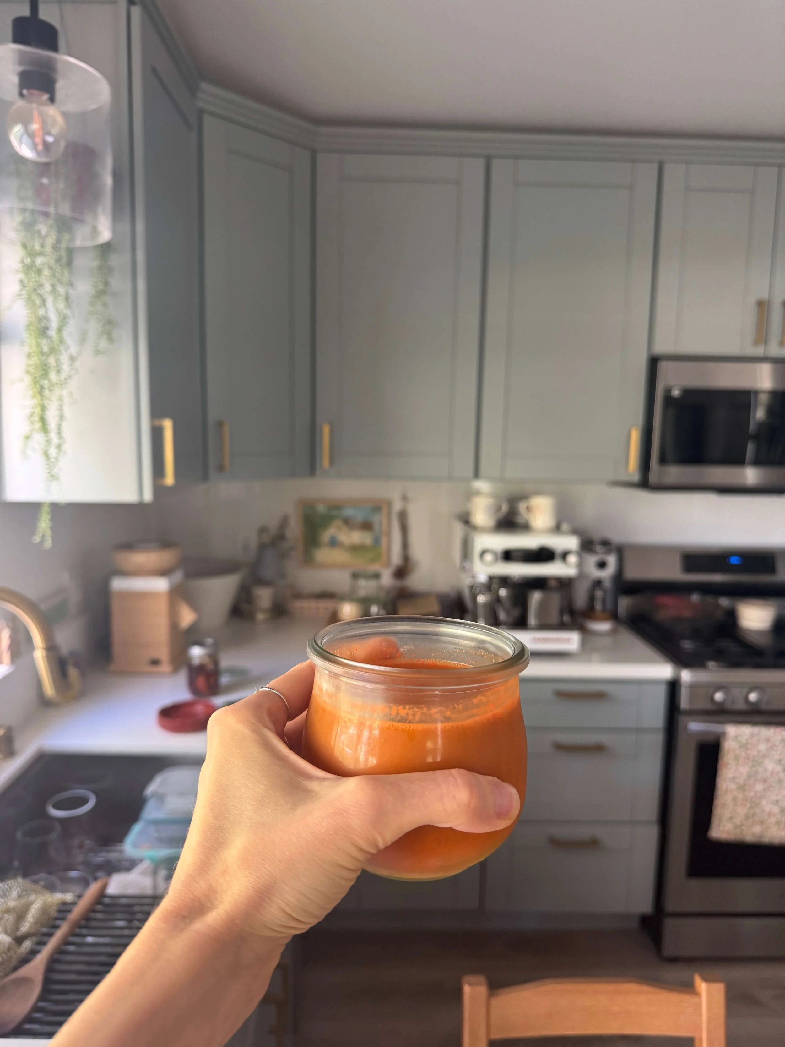 hand holding glass carrot juice in kitchen blue counter background