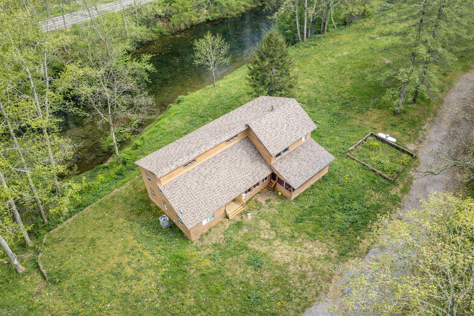 A multi-story wooden house with a screened porch, situated in a rural area with trees and fallen autumn leaves on the ground.