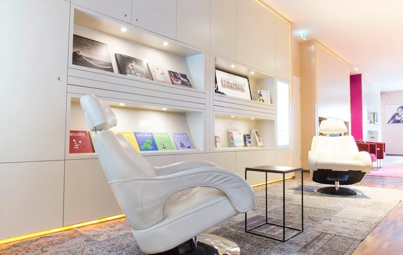 Modernes Wartezimmer mit weißen Sesseln, Bücherregalen, dekorativen Bildern und warmer Beleuchtung.