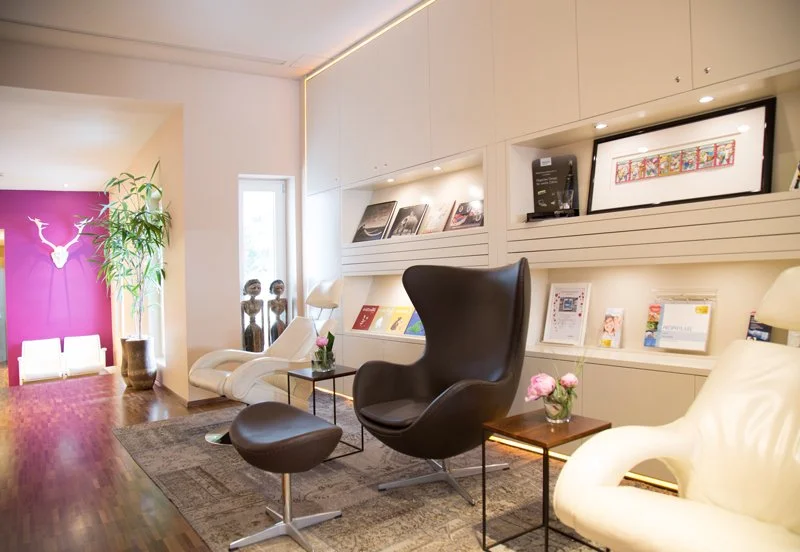 Modernes Wartezimmers mit schwarzen und weißen Relaxsesseln, weißen Bücherregalen, Pflanzen und moderner Dekoration.