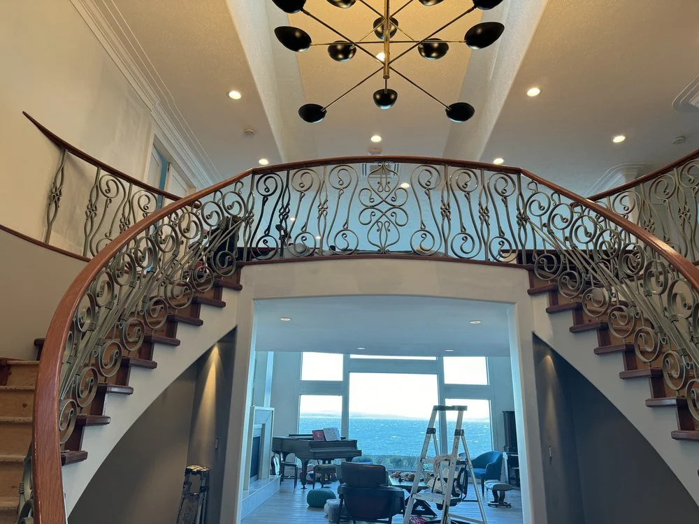Recessed pot lights and a modern chandelier over a curved staircase in an Oak Bay home
