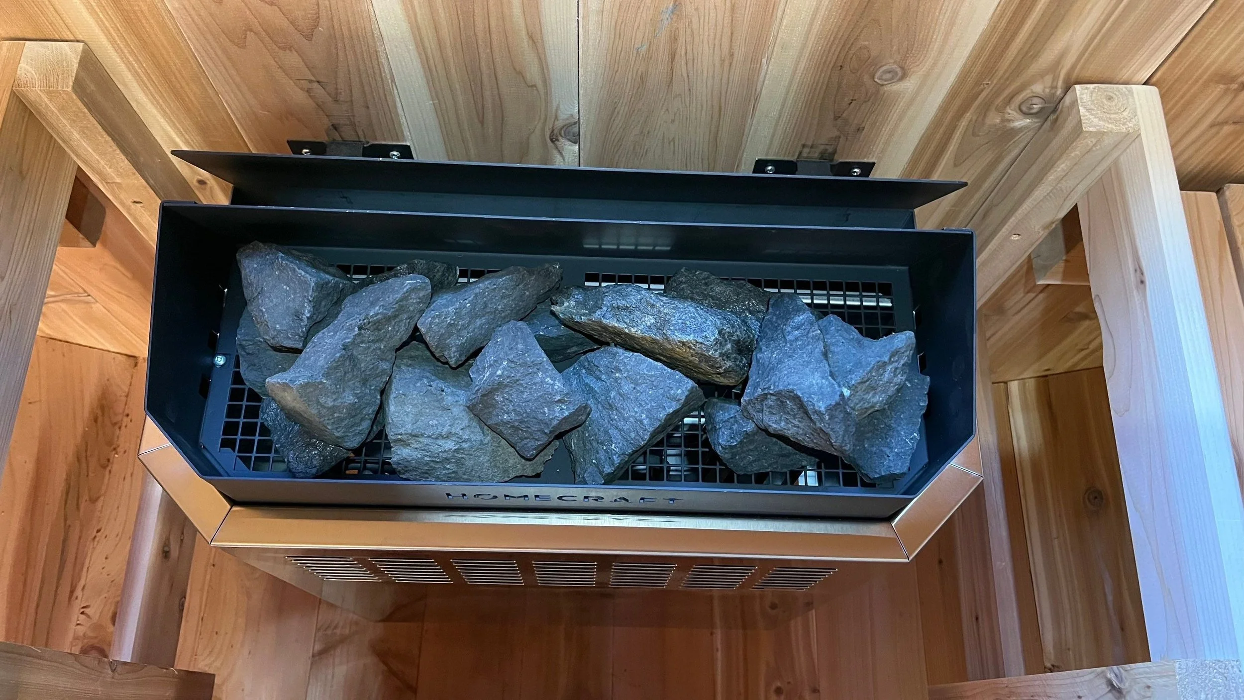 Homecraft 9kW electric sauna heater with igneous sauna stones loaded in the basket, cedar interior