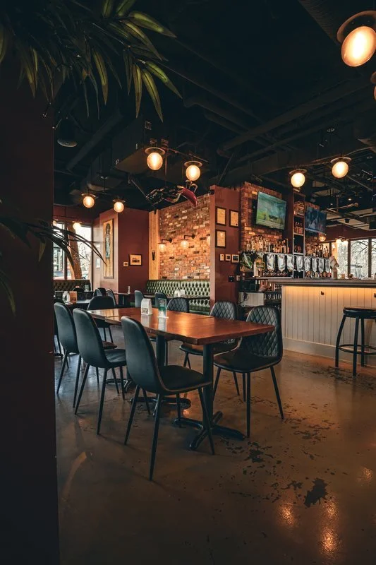 Warm pendant lighting over pub dining tables with illuminated bar and beer taps behind