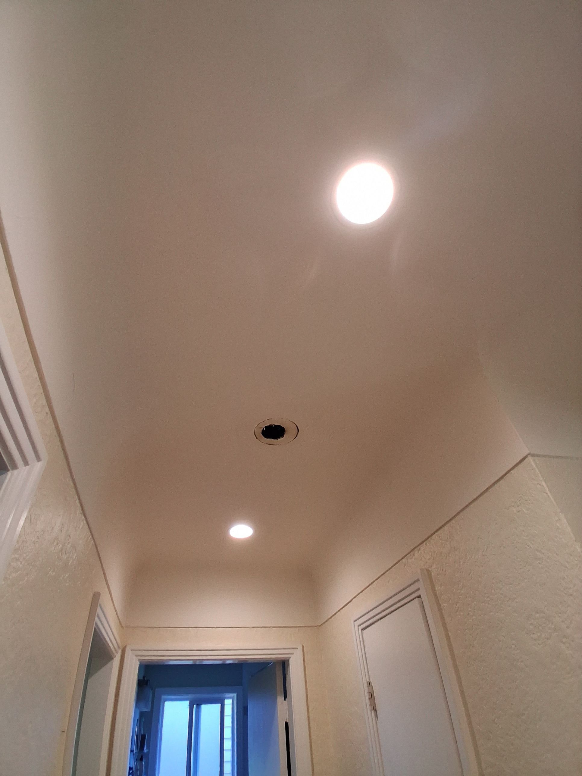 Recessed LED pot lights installed down a hallway ceiling, one fixture still being fitted