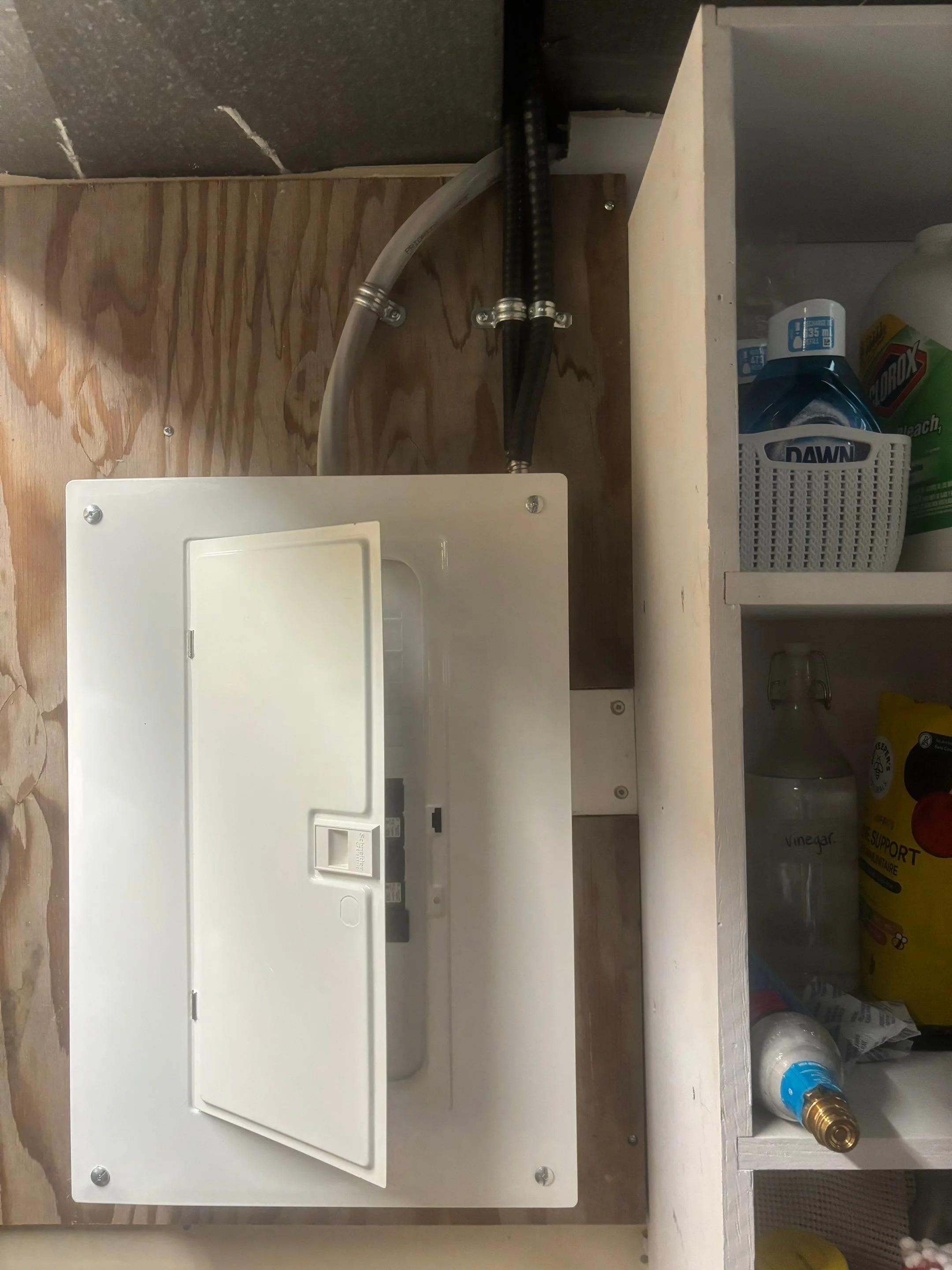 Closed electrical sub-panel in a laundry area with the new heat pump circuit exiting the top