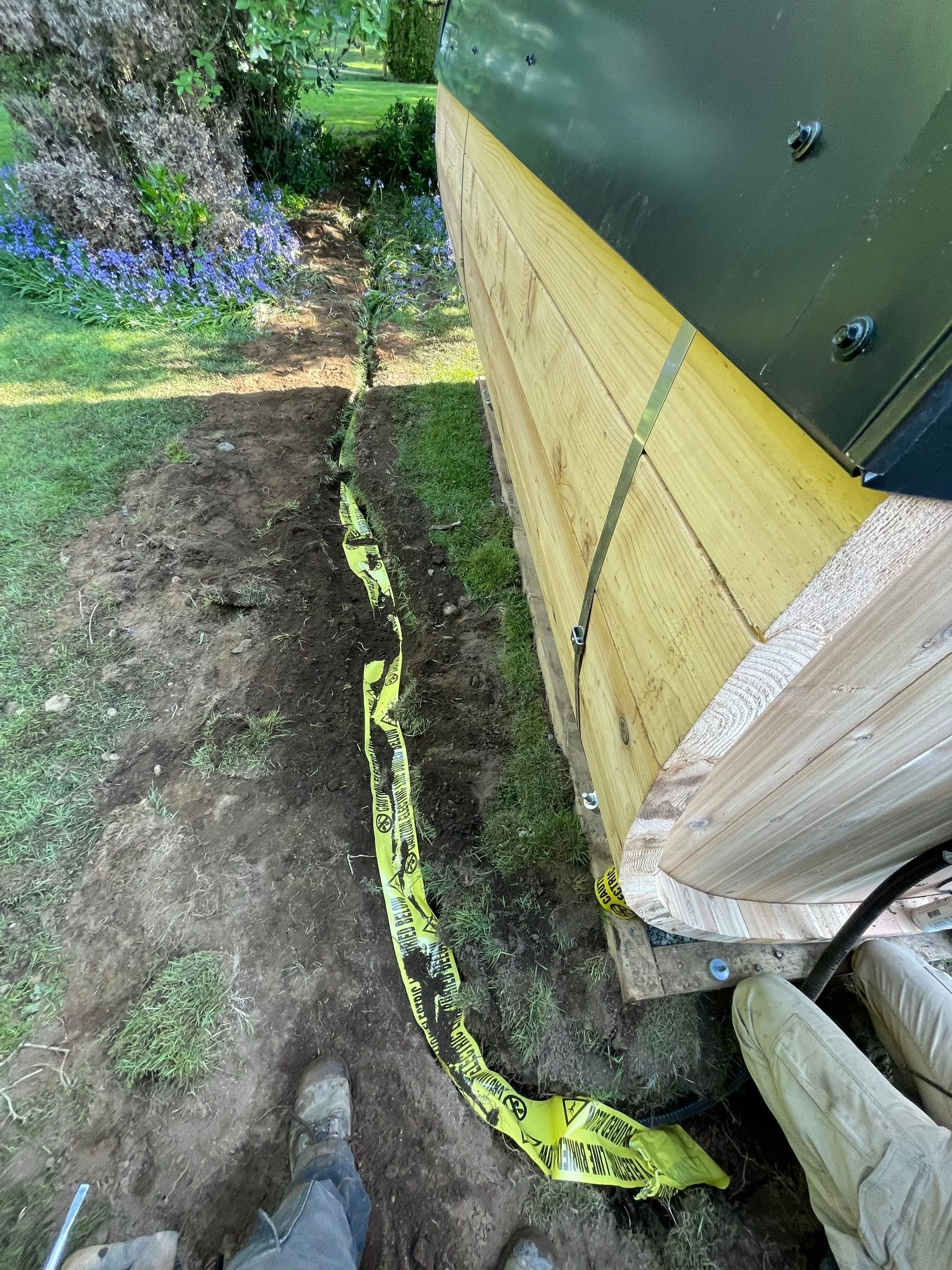 Trench dug across a Saanich yard with buried electric line warning tape laid over the sauna feeder cable