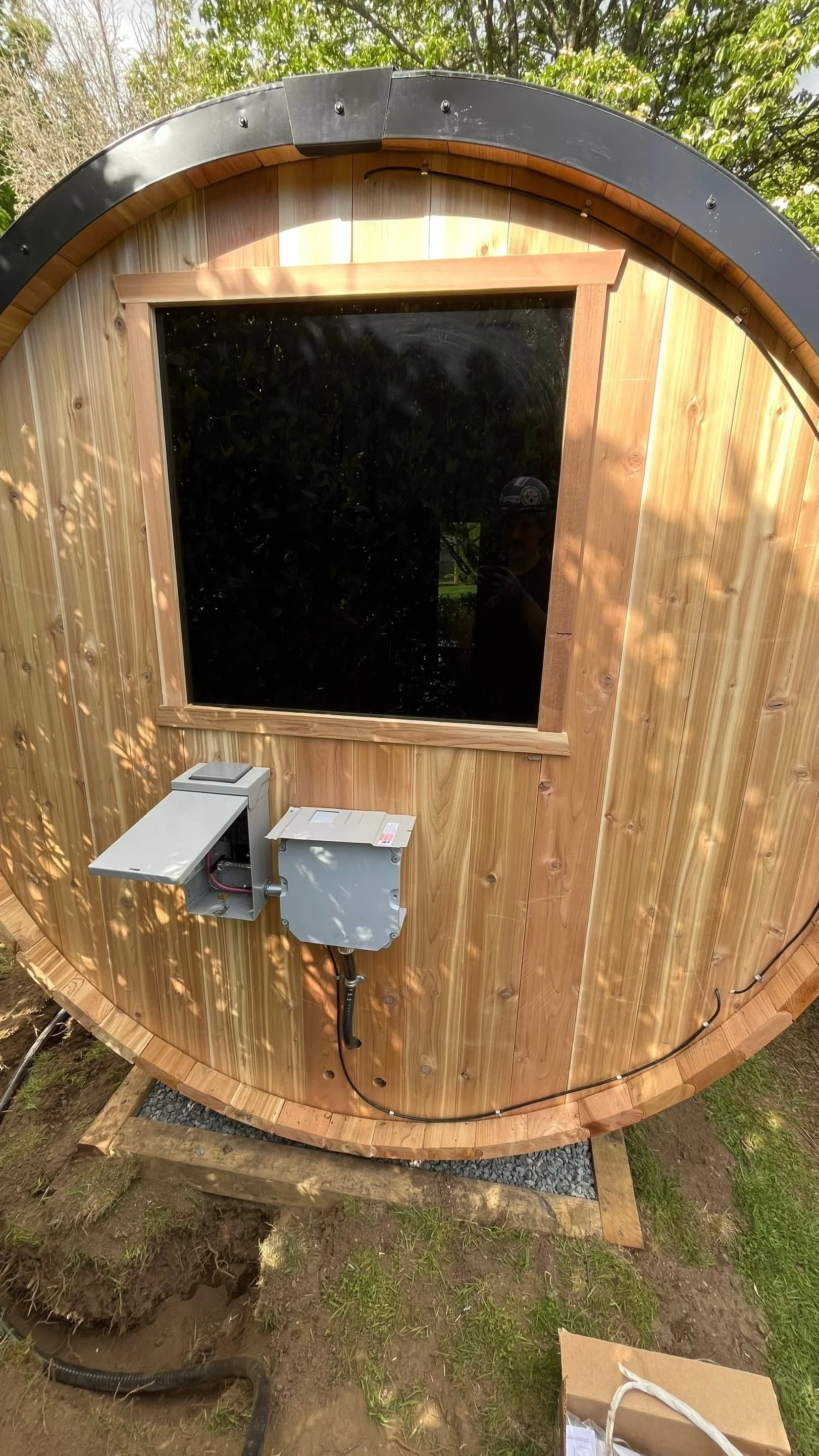 Outdoor cedar barrel sauna with a weatherproof subpanel and disconnect mounted on the exterior wall