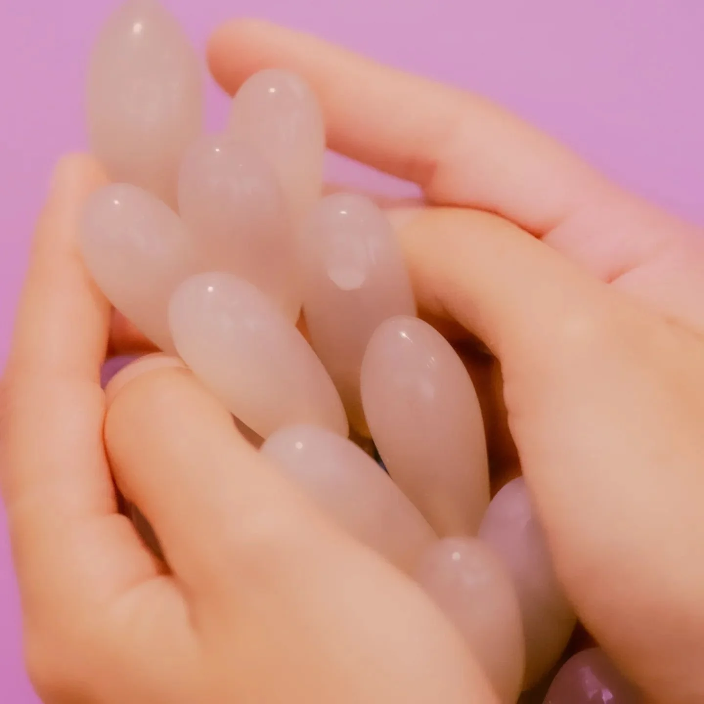 Hand holding translucent eggs with pink background