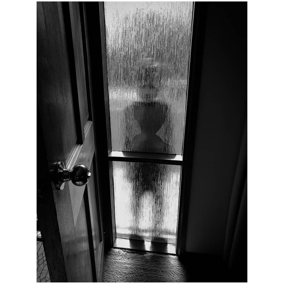 Silhouette of a person standing outside a door with frosted glass pane, creating a shadowy figure.