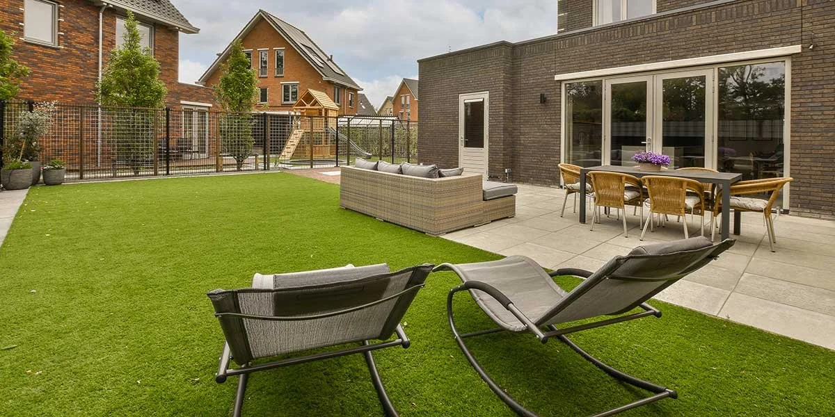 Landscaped residential backyard with vibrant artificial turf, a paved patio, and modern outdoor dining furniture.