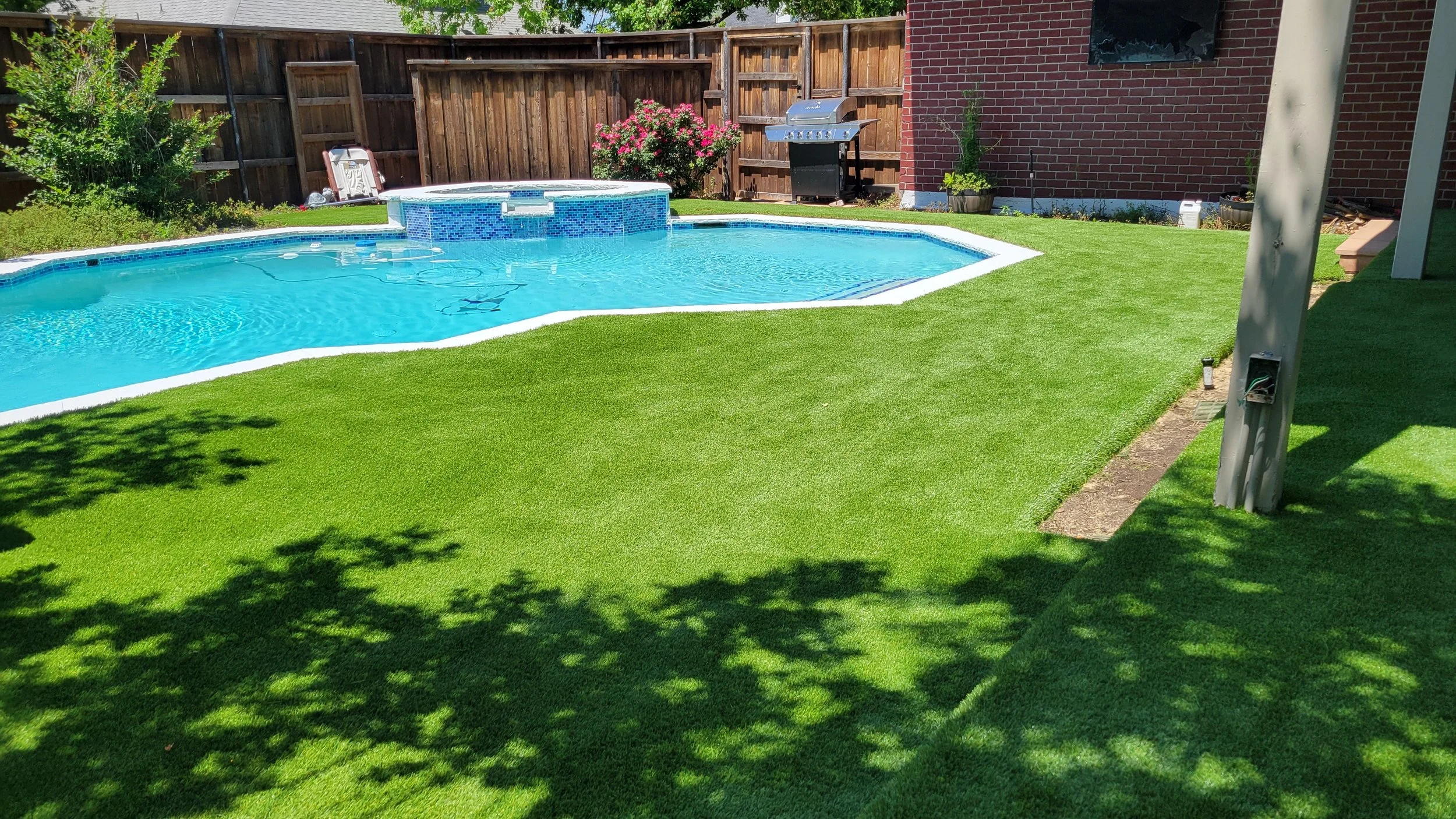 Residential pool area with custom artificial turf and stone coping in Dallas-Fort Worth, showcasing a low-maintenance backyard design by Total Turf Works.