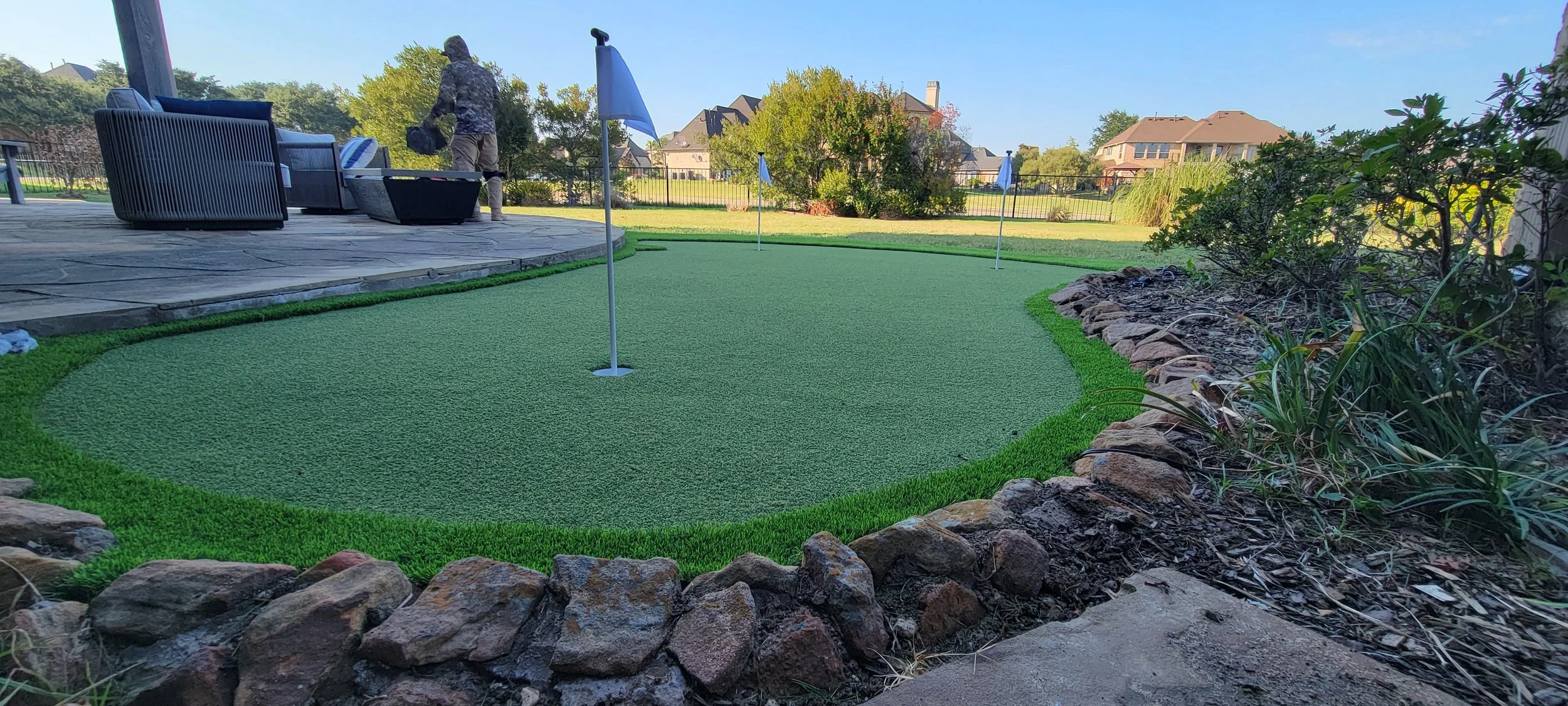 Residential backyard featuring professionally installed artificial turf by Total Turf Works, with stone edging and landscaped garden areas.