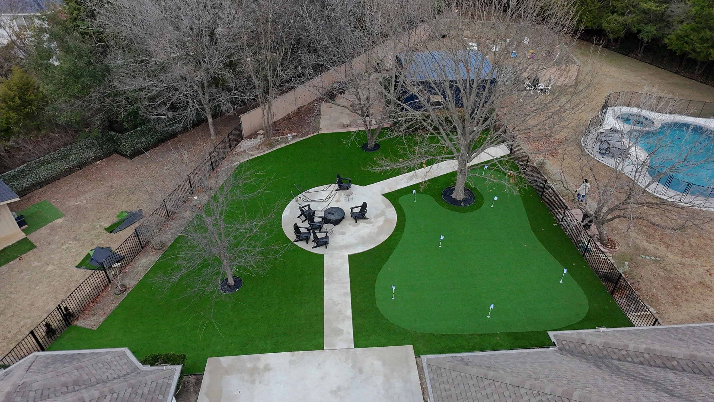 Aerial view of a custom backyard putting green and stone fire pit patio with premium artificial turf installation in the Dallas-Fort Worth area.