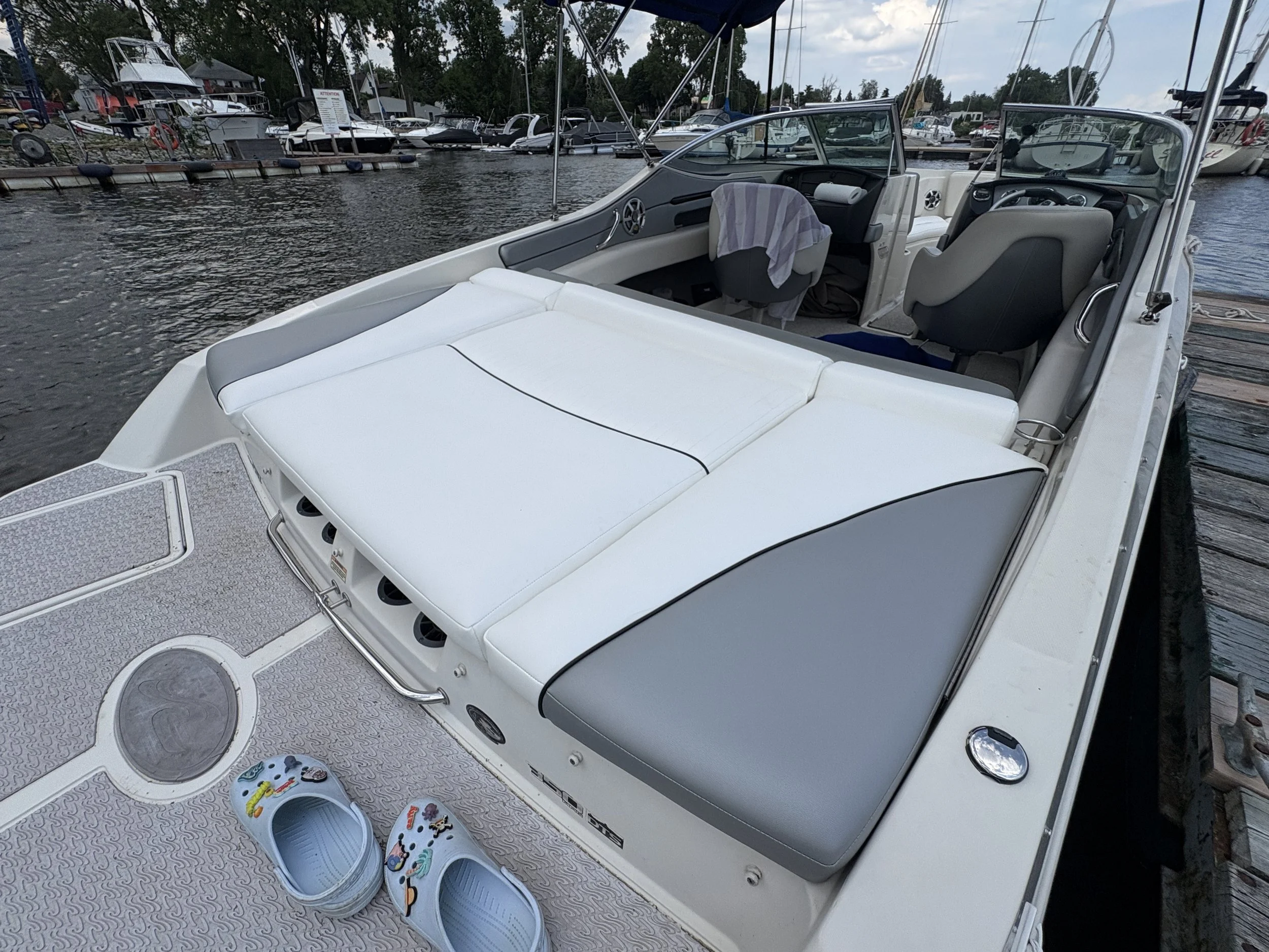 View of a boat docked at a marina with a boat's interior visible, including a towel on the seat, and multiple other boats docked in the background on a cloudy day.