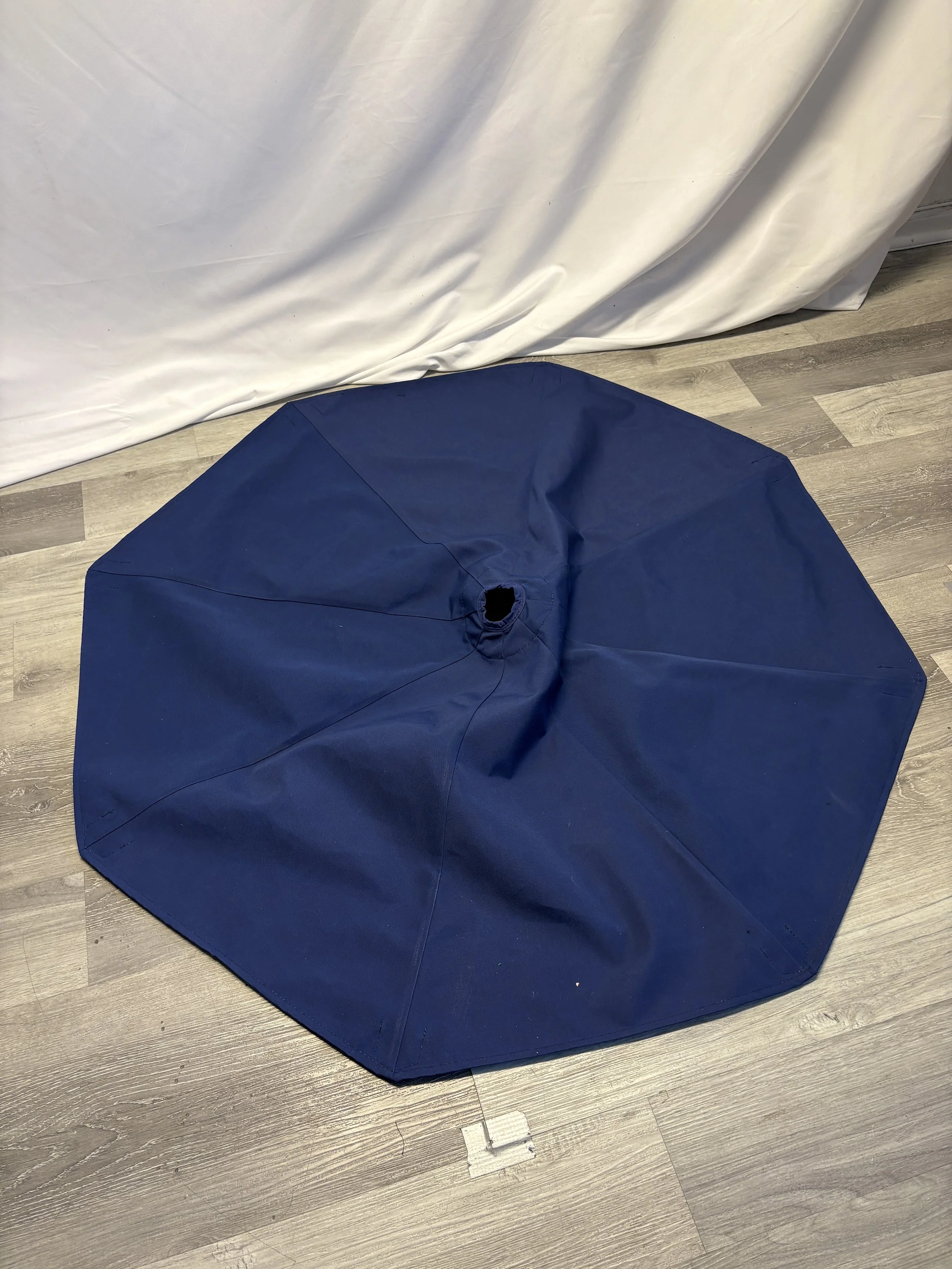 A blue umbrella lying open on a wooden floor next to a white curtain.