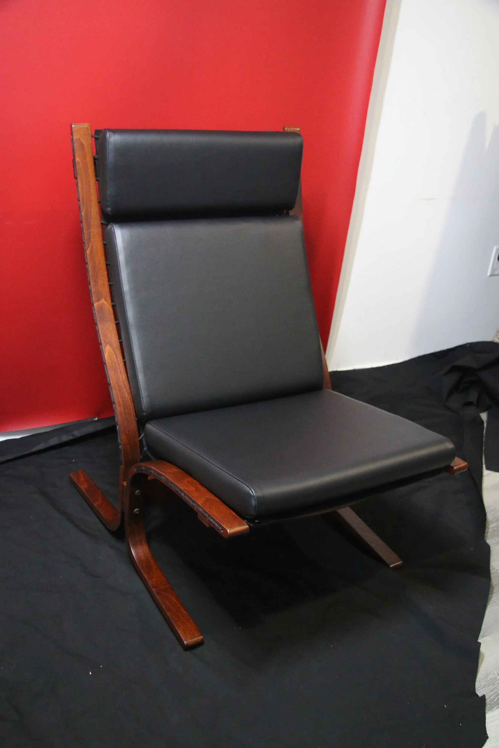 A black leather chair with a wooden frame and a headrest, positioned against a red and white wall on a black surface.