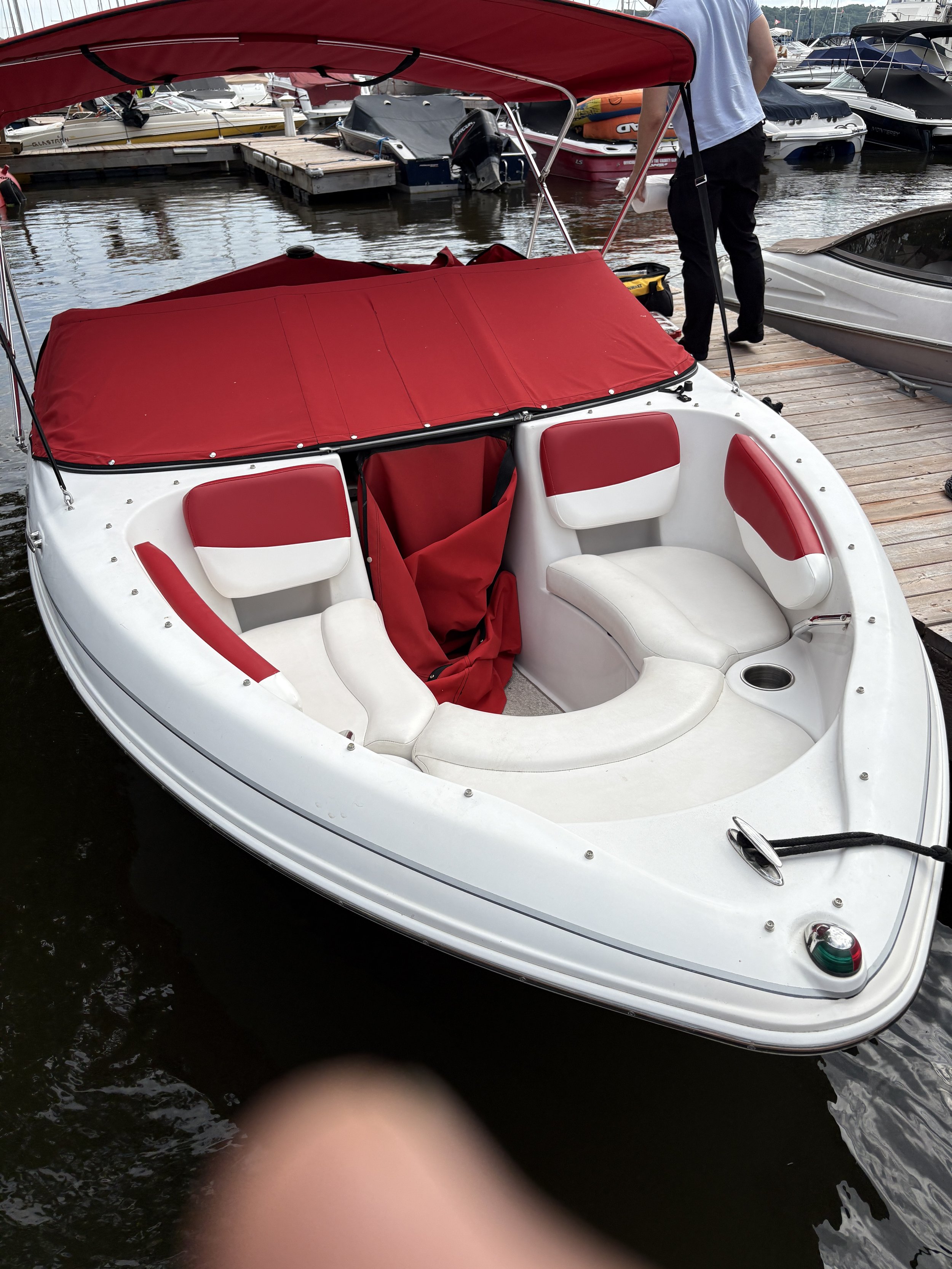 A small white boat with red seating and a red cover docked at a marina with other boats in the background.
