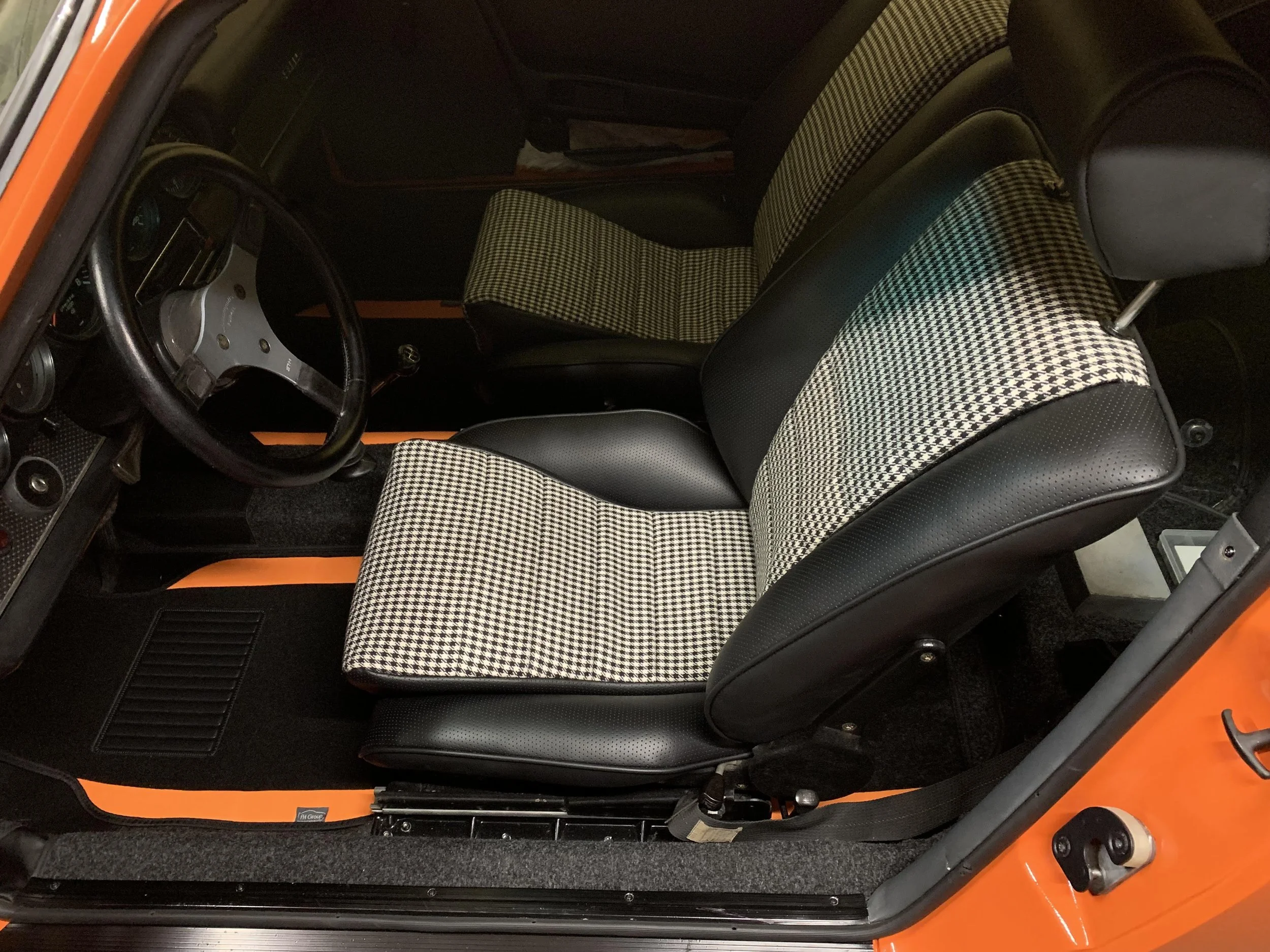 The interior of a vintage car showing black and white checkered cloth seats, a black steering wheel, and a dashboard with gauges.