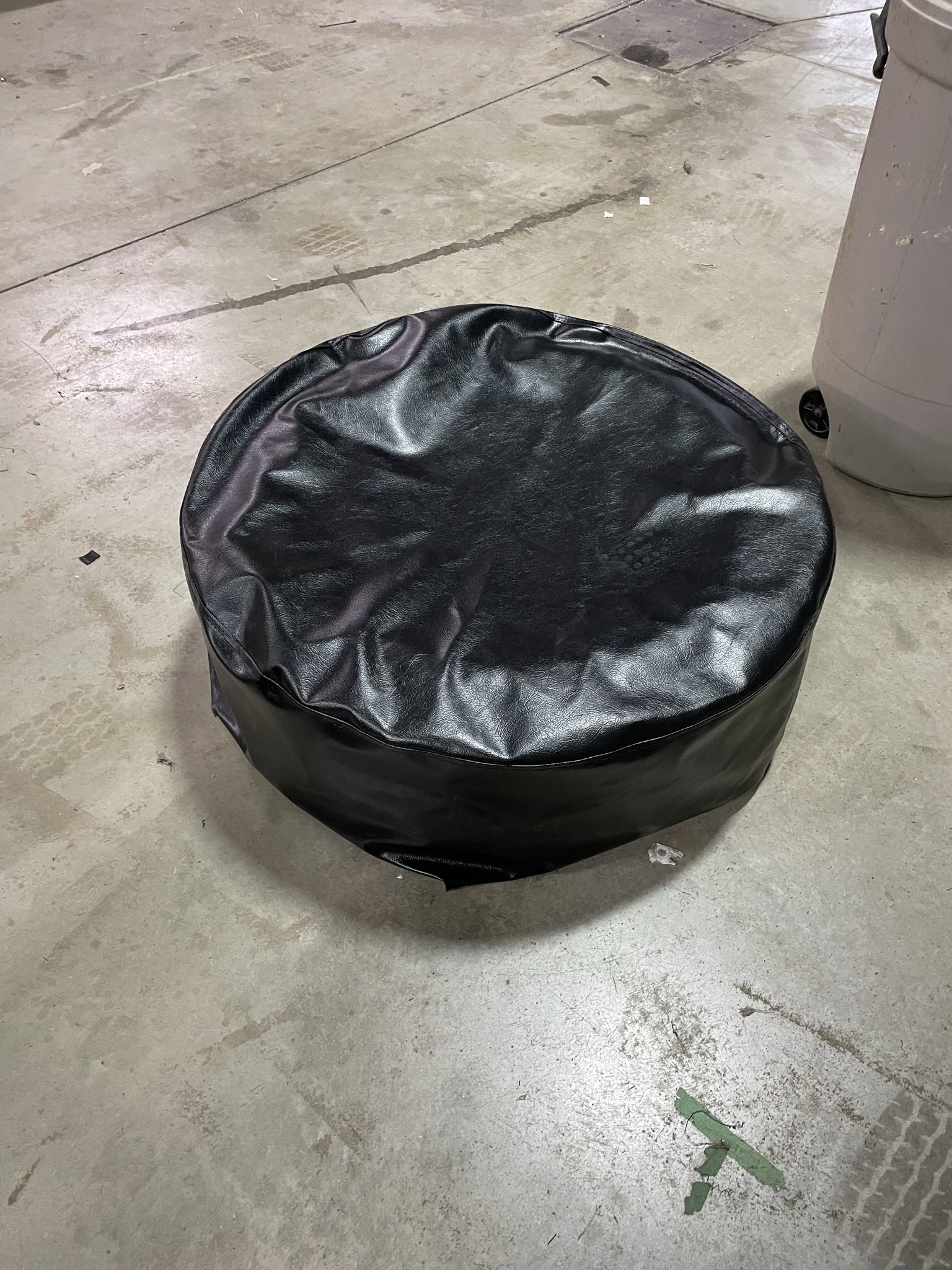 Black leather pouf on a concrete floor in an industrial setting.