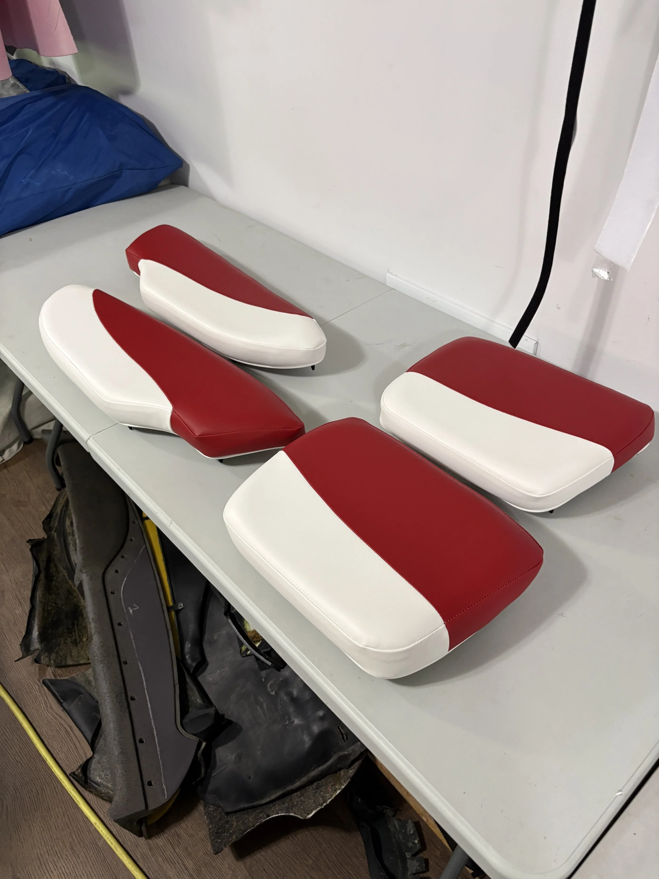 A pair of red and white ice skate boots resting on a white table, with a blue bag and some luggage visible beside them.