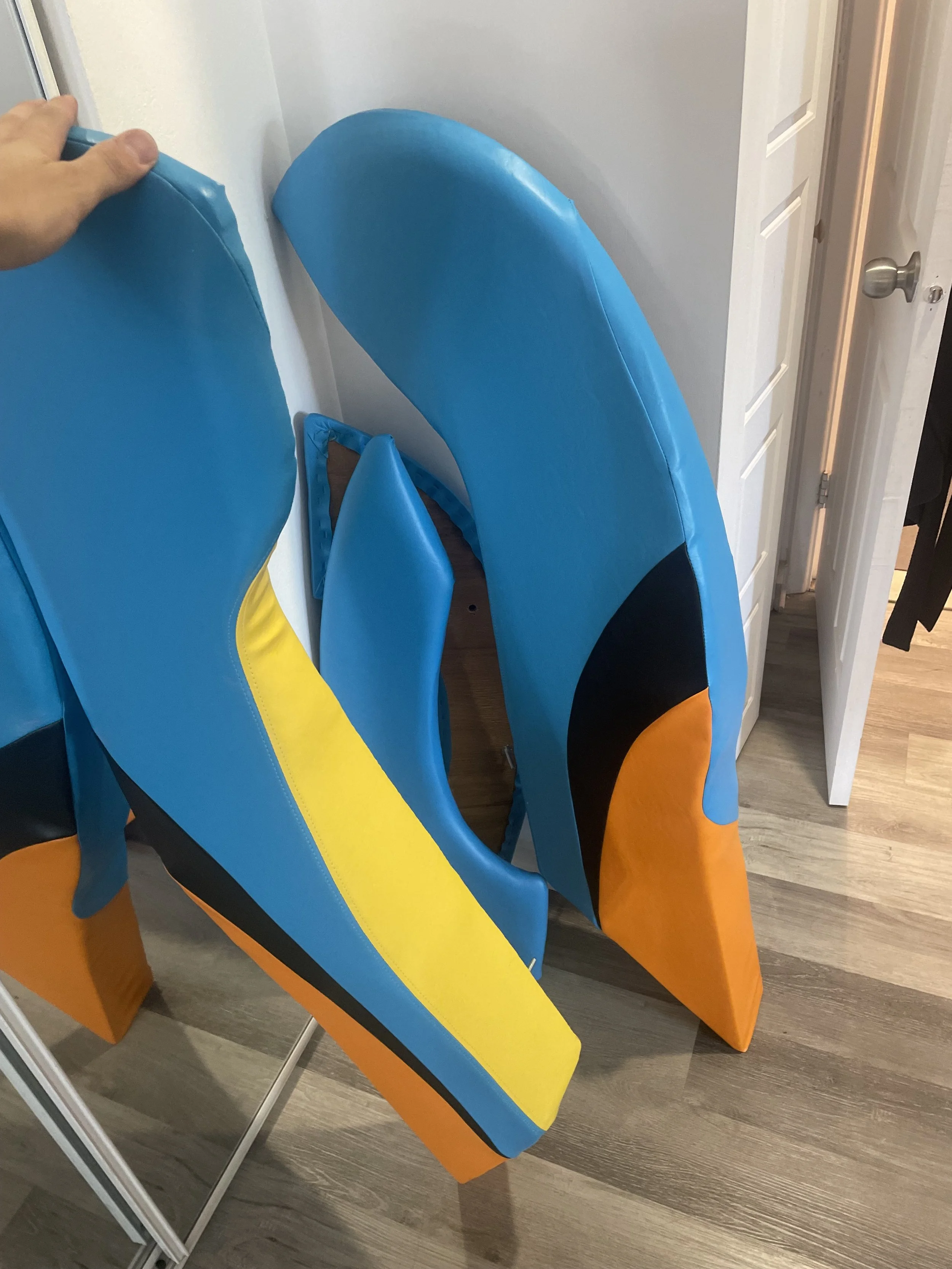 Colorful surfboard-shaped padded cushions in blue, yellow, black, and orange leaning against a wall near a door.