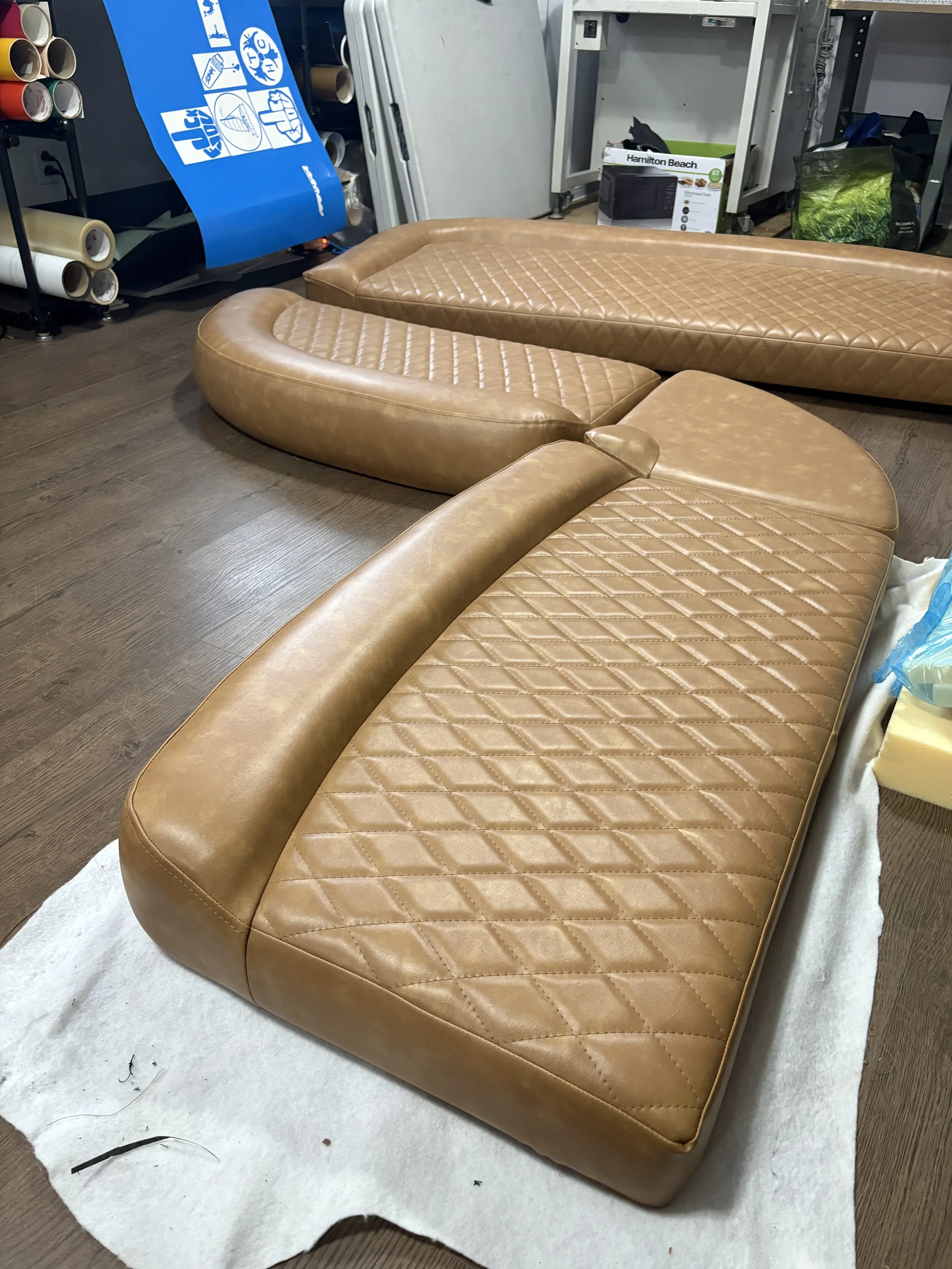 Brown leather tufted sectional sofa placed on a white blanket on a wooden floor, with design quilted pattern on the cushions.