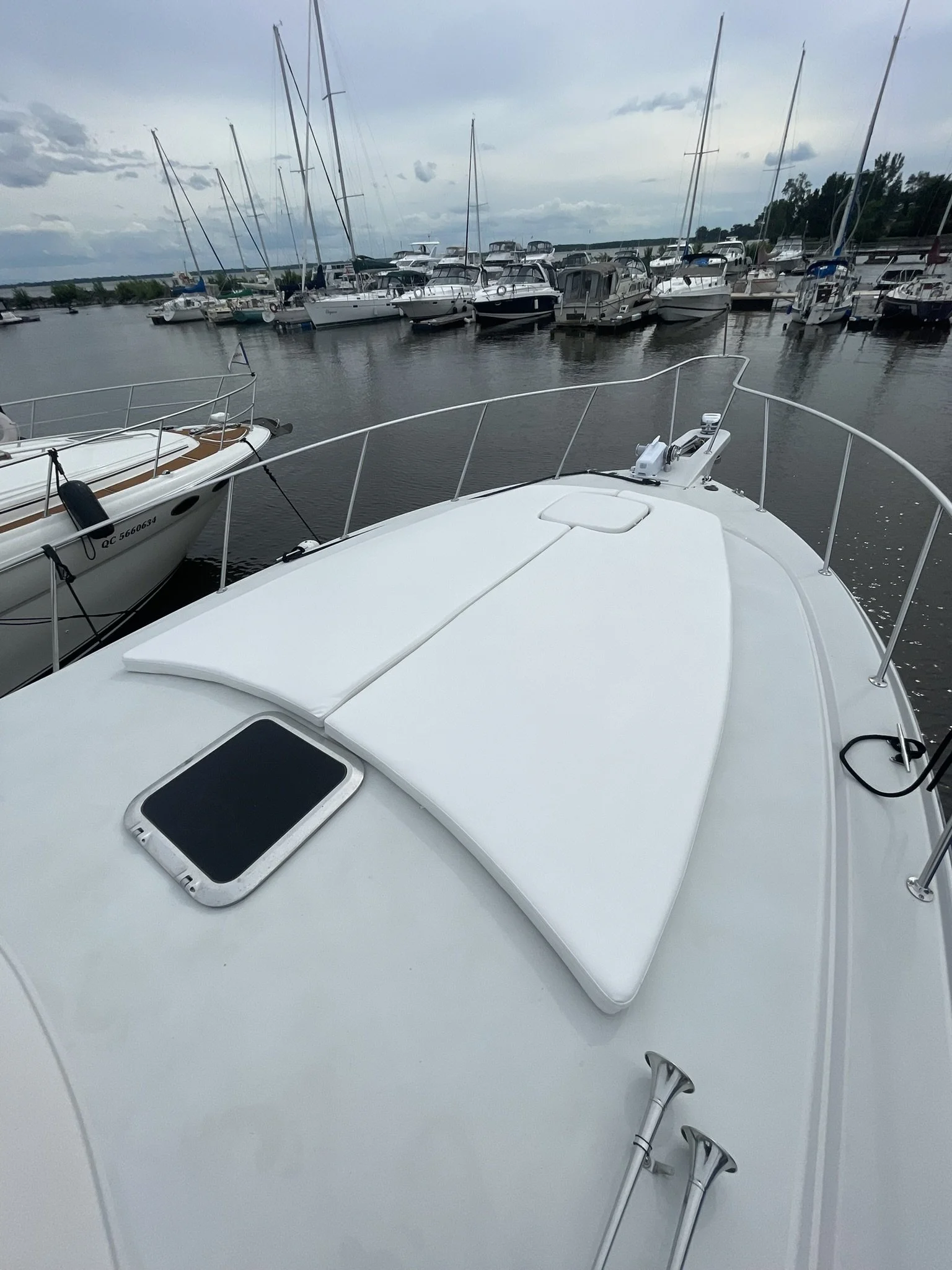 View from the deck of a white boat looking at a marina with numerous boats docked in the water and cloudy sky overhead.