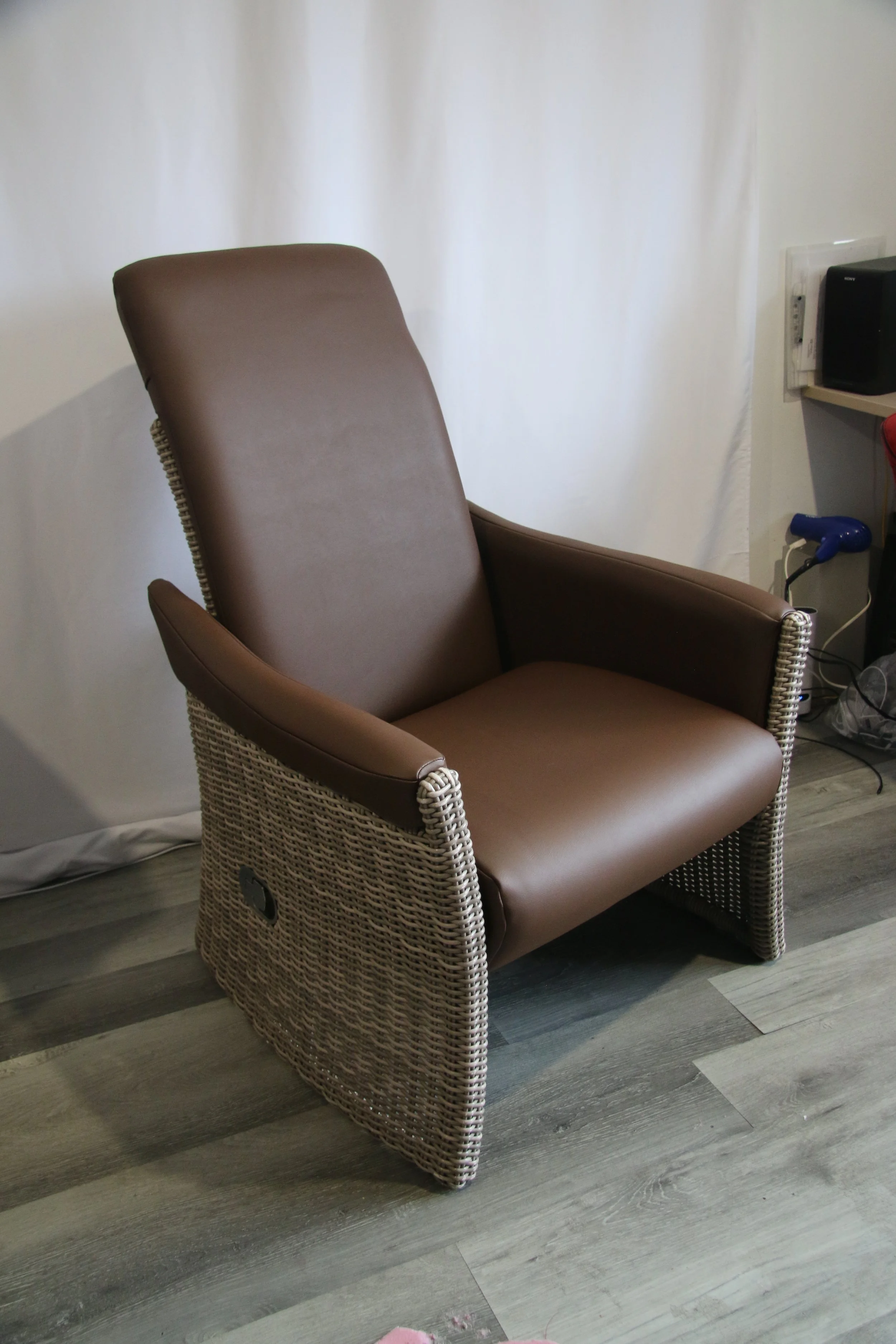 A brown high-back armchair with woven sides situated on a grey wooden floor against a white backdrop.