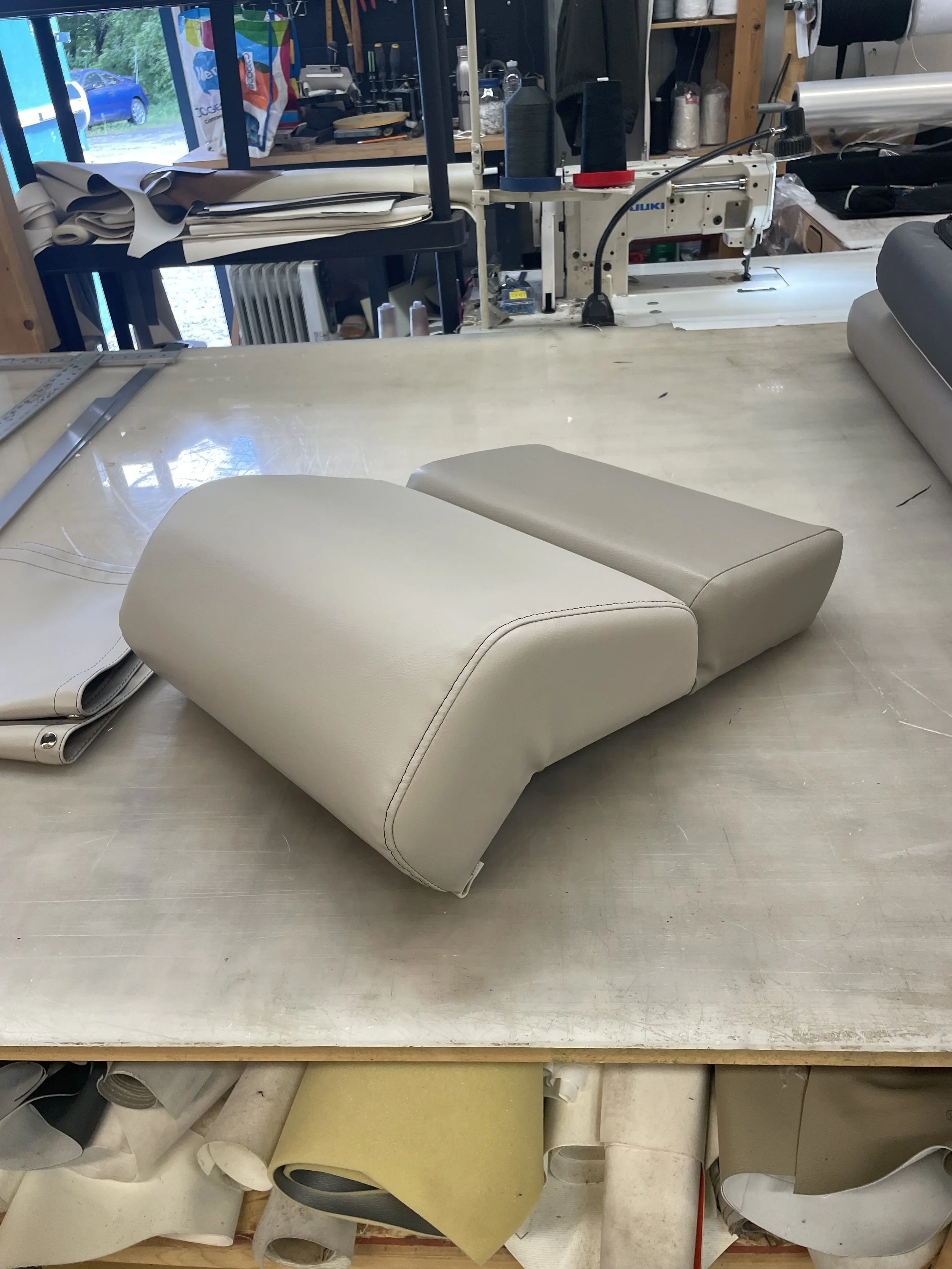 An upholstery work area featuring a sewing machine, rolls of fabric, and partially covered cushions on a worktable.