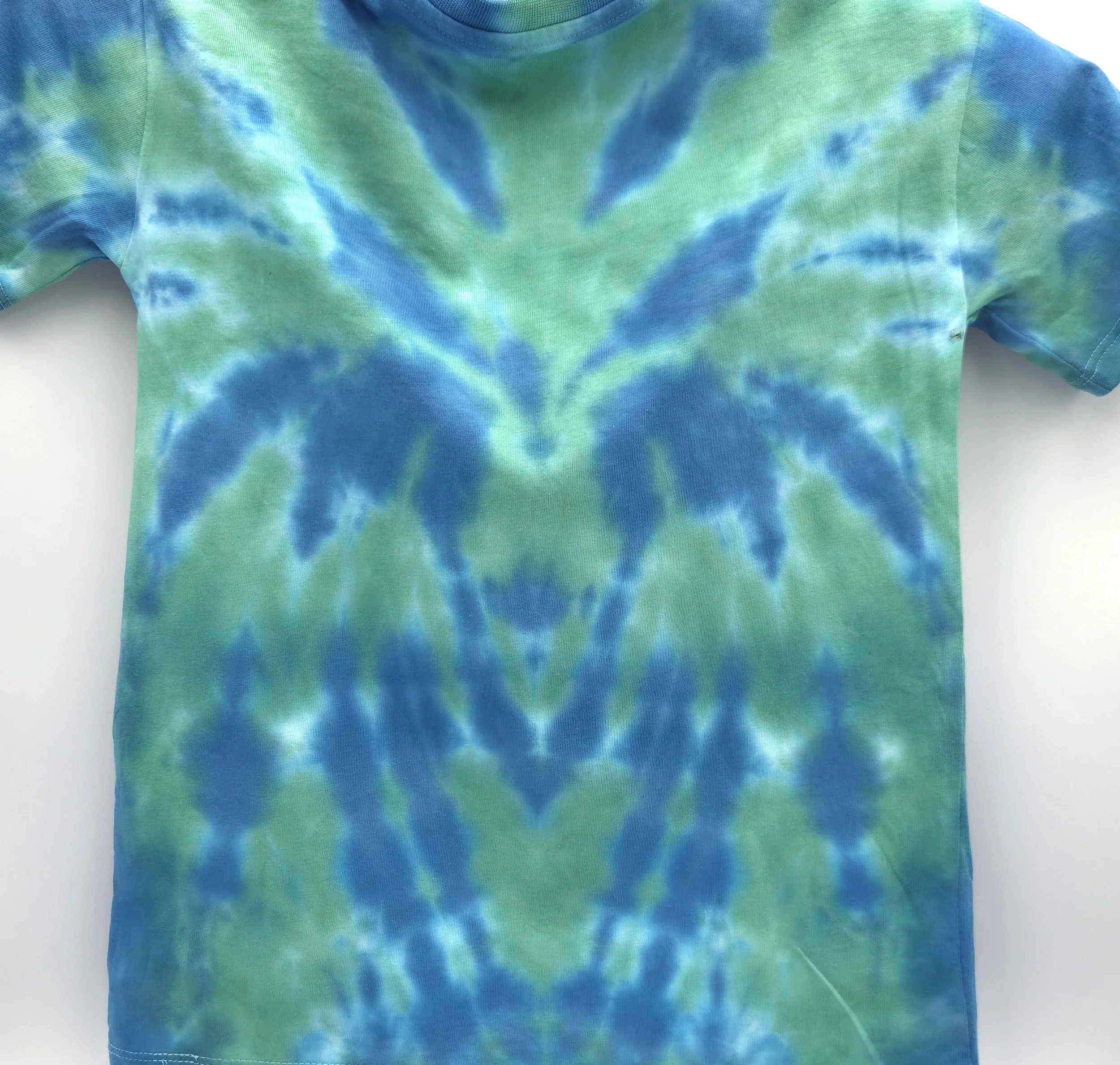 close up of A child's light green t-shirt displaying a central sky blue tie-dye spider pattern, back view