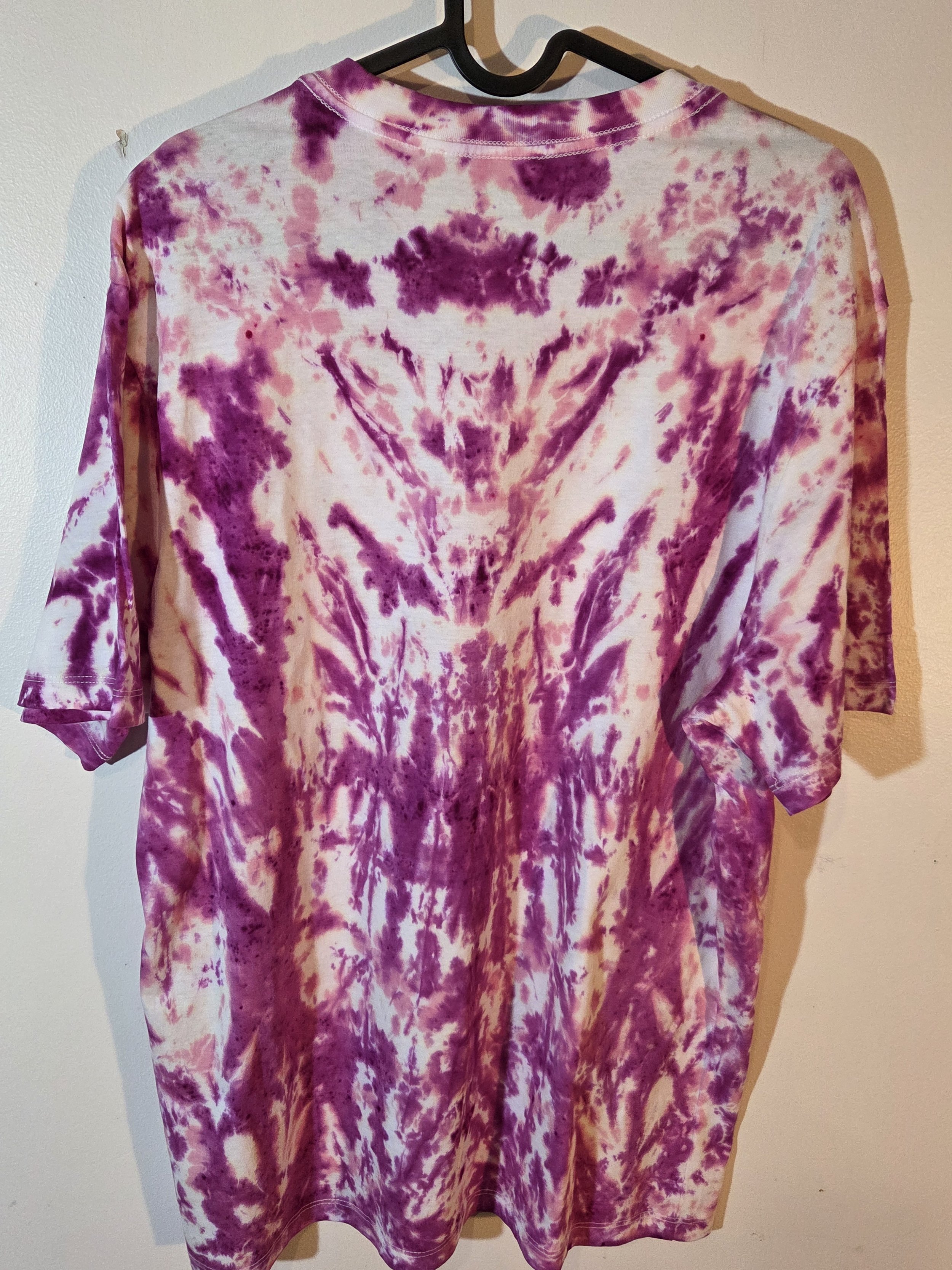 A large adult white t-shirt featuring a tie-dye pattern of a deep wine feathery central motif against an abstract pink background.