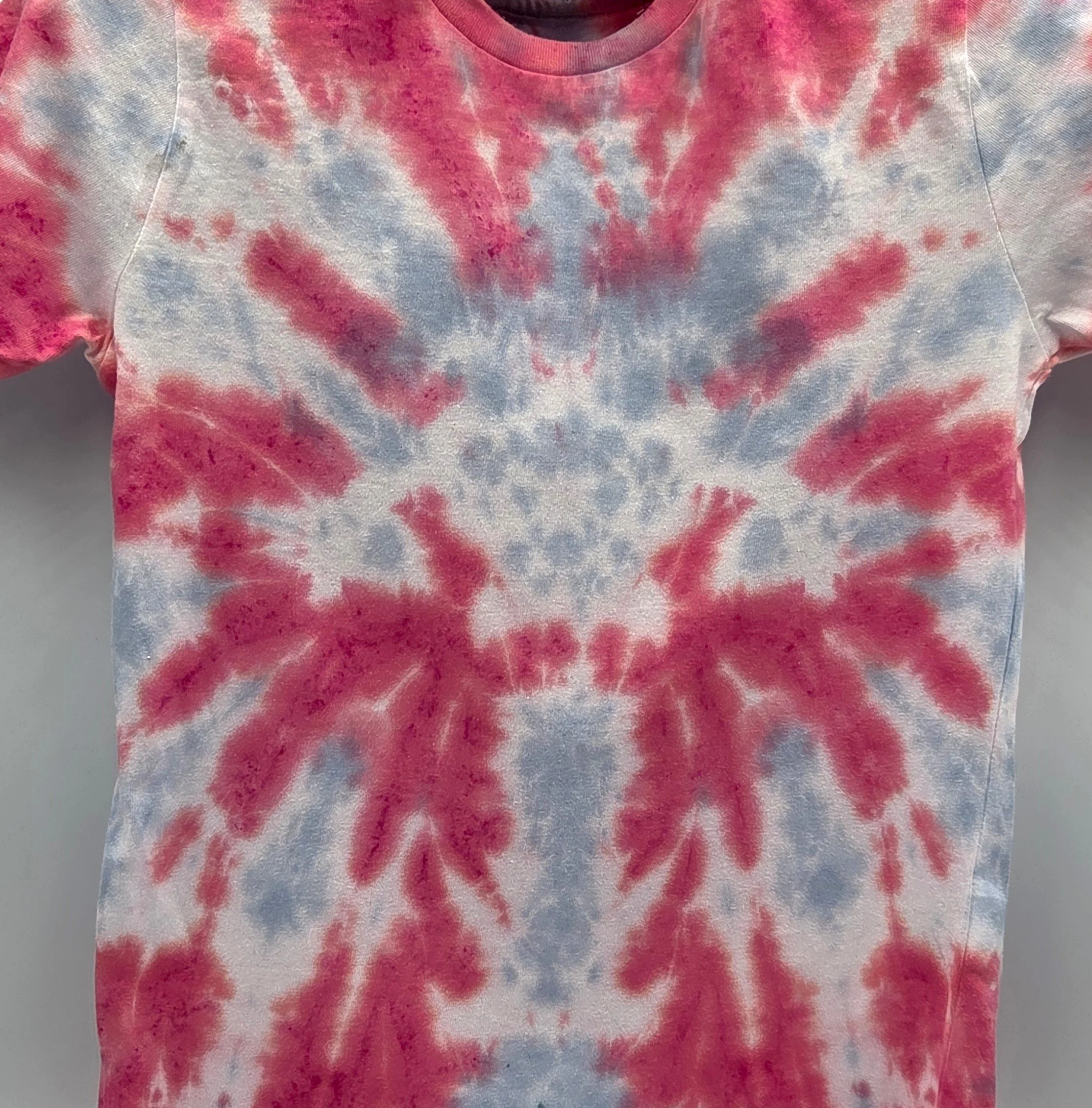 close up of a child's red t-shirt. A central pale grey tie-dye pattern resembles a large webbed flower.