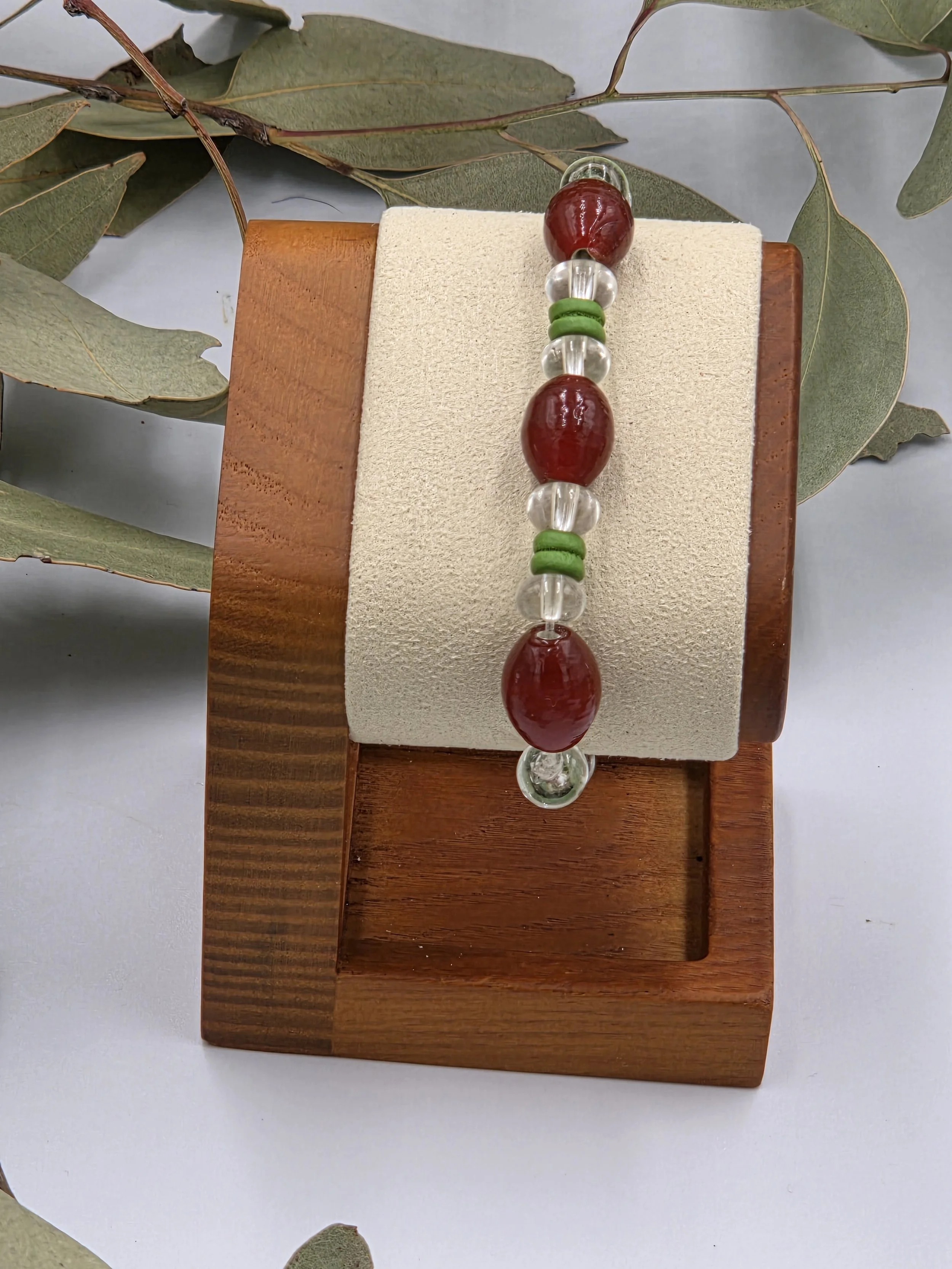 Rust red glass oval beads separated by clear glass donuts and forest green ribbed wood beads on an elastic bracelet.