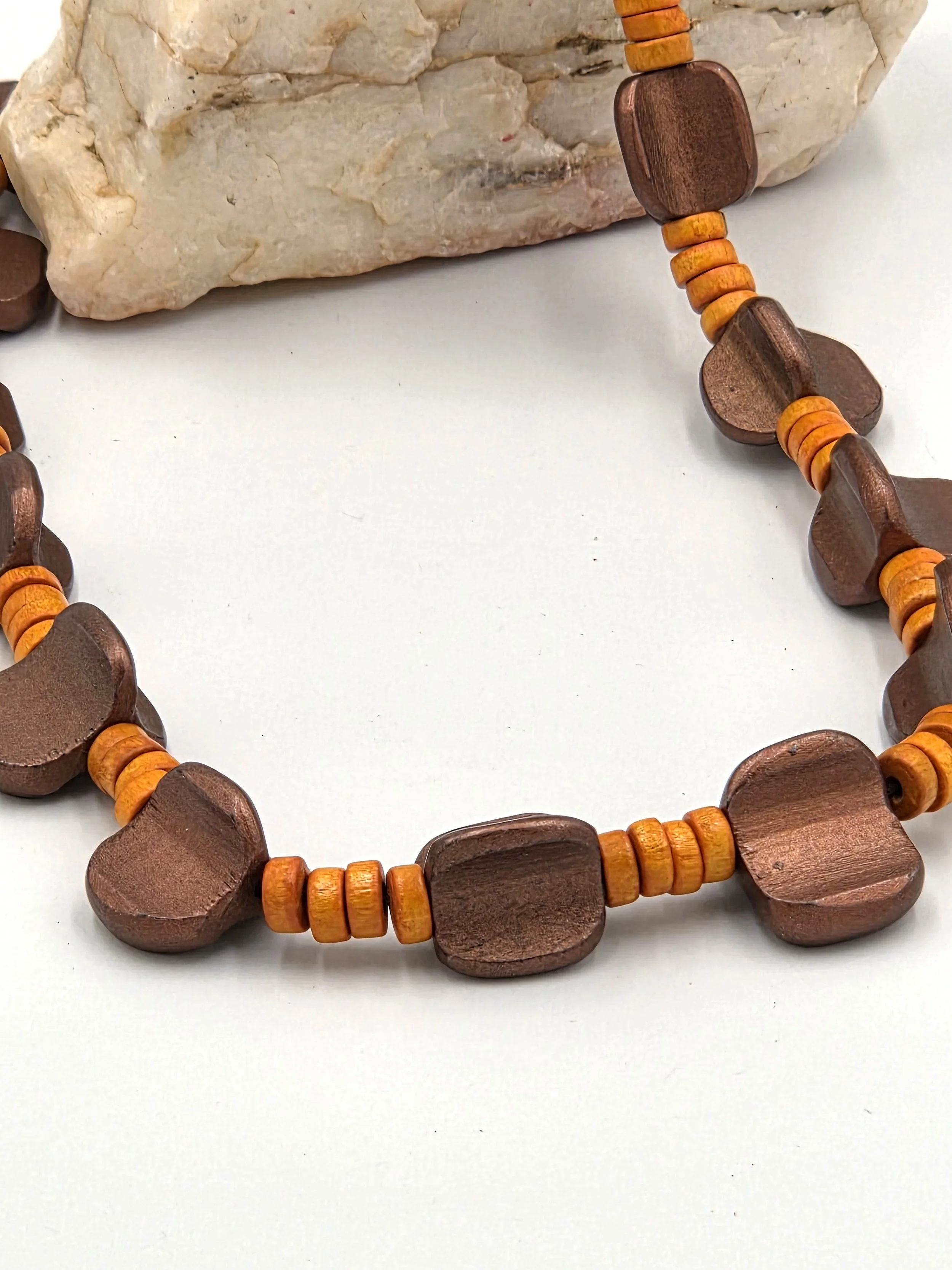 closeup of Bronze asymmetric wood beads and orange disc beads on a 48cm necklace.