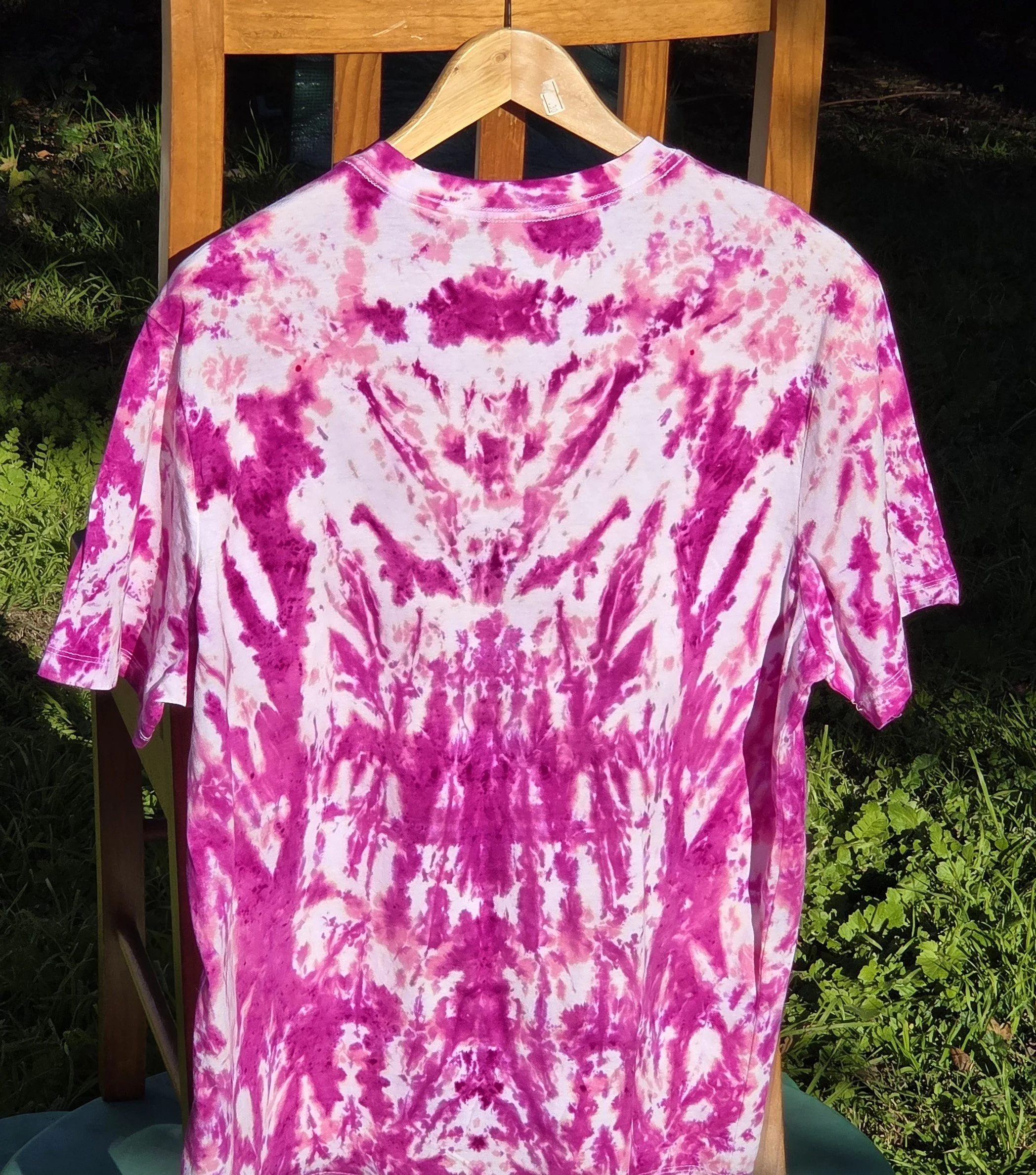 back view of A large adult white t-shirt featuring a tie-dye pattern of a deep wine feathery central motif against an abstract pink background.