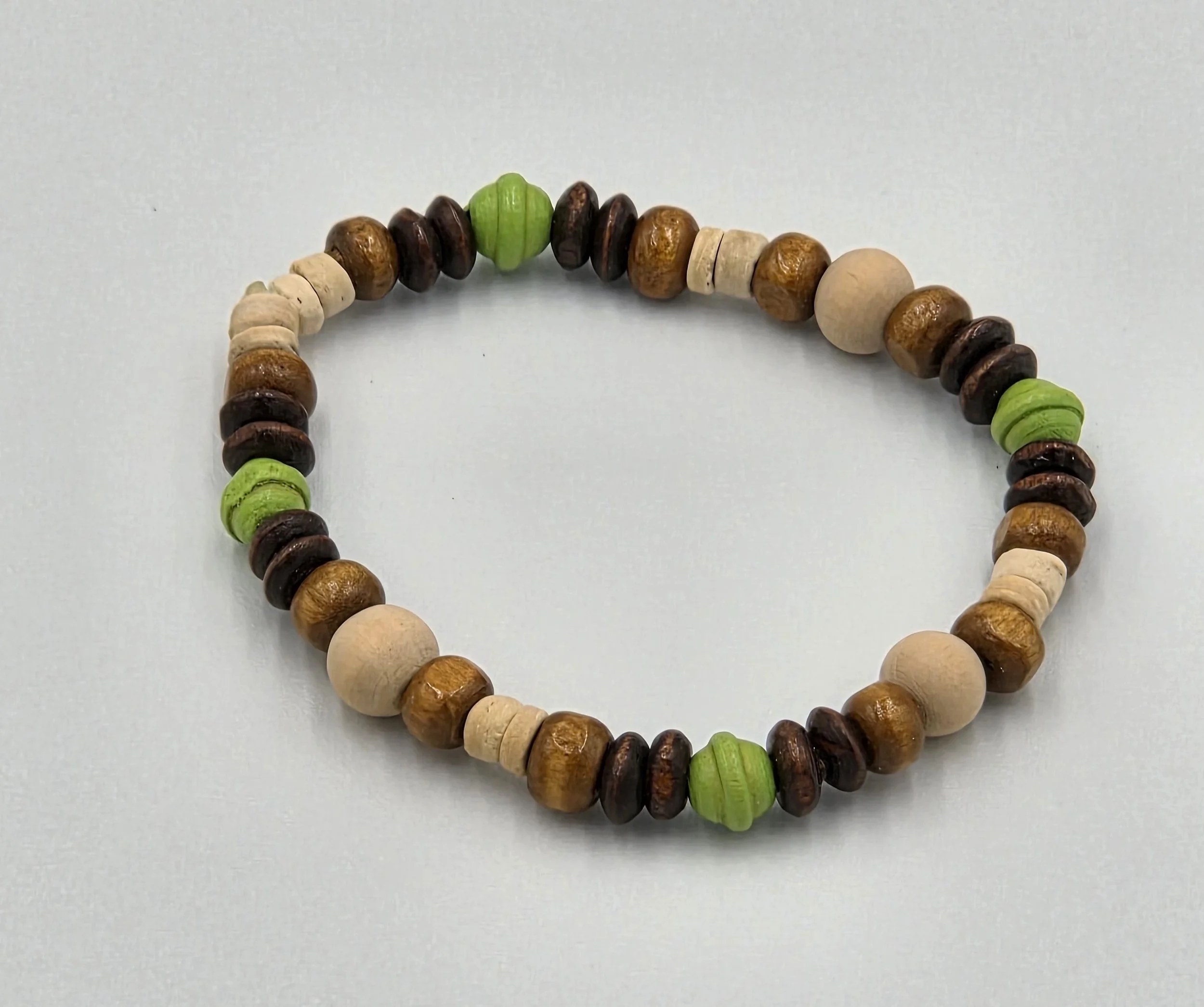 Small elastic bracelet with cream, brown, and lime green wooden beads in varied shapes.