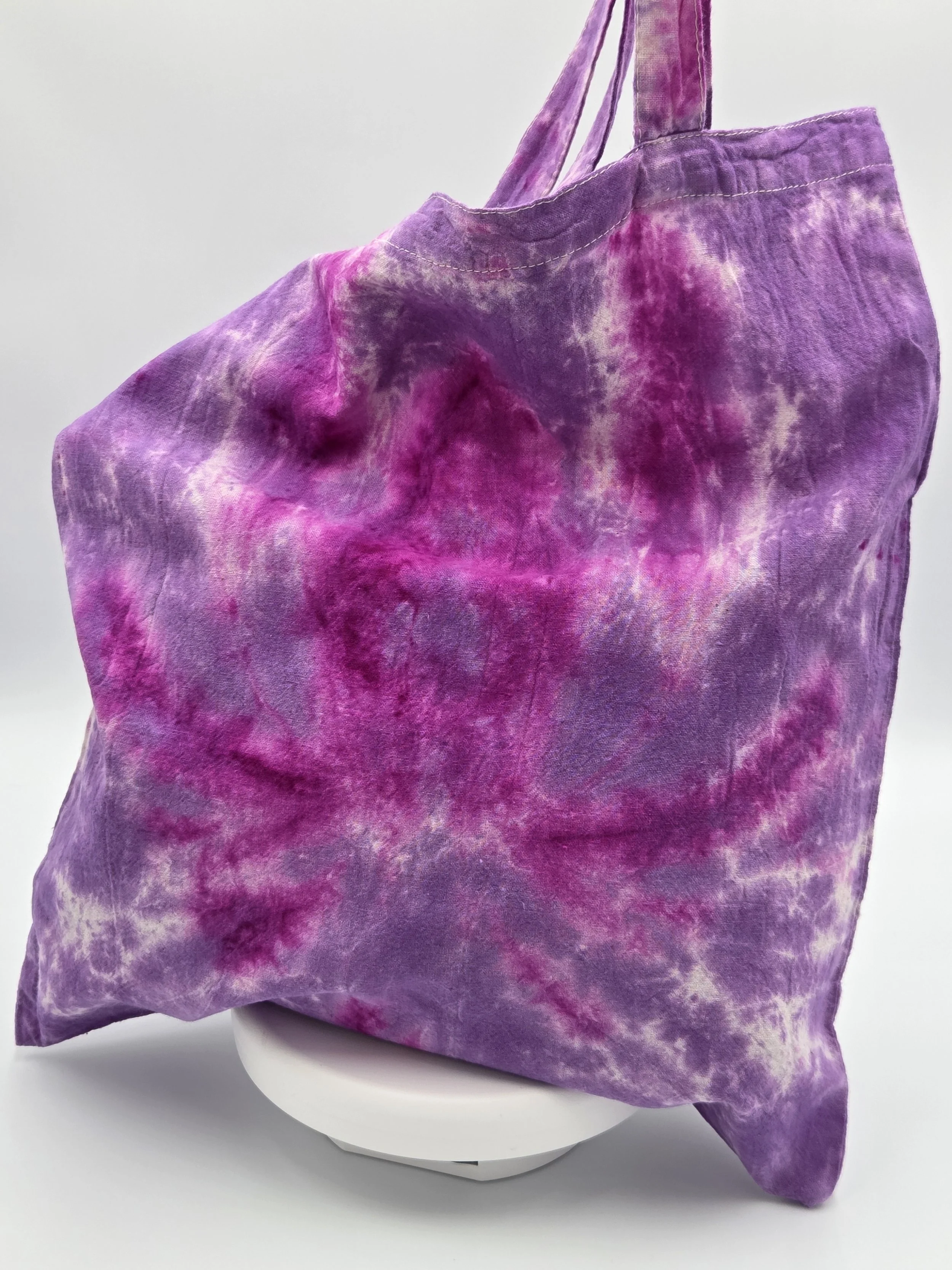 A calico tote bag featuring a tie-dye lotus flower pattern in deep fuchsia resting against a rich purple and white background.