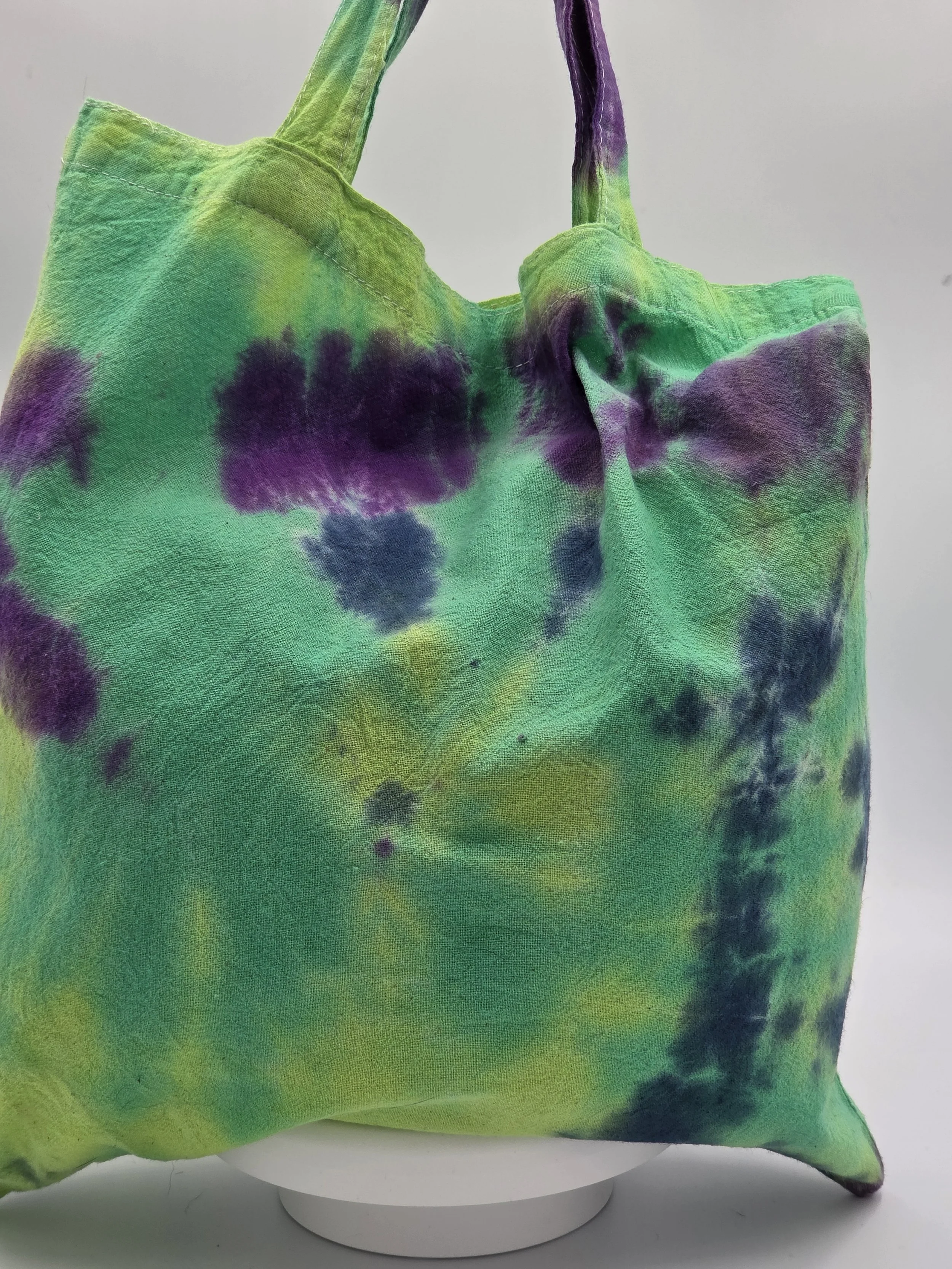 A calico tote bag featuring an abstract dark blue and purple half-circle tie-dye pattern against a lime green and pastel yellow background.