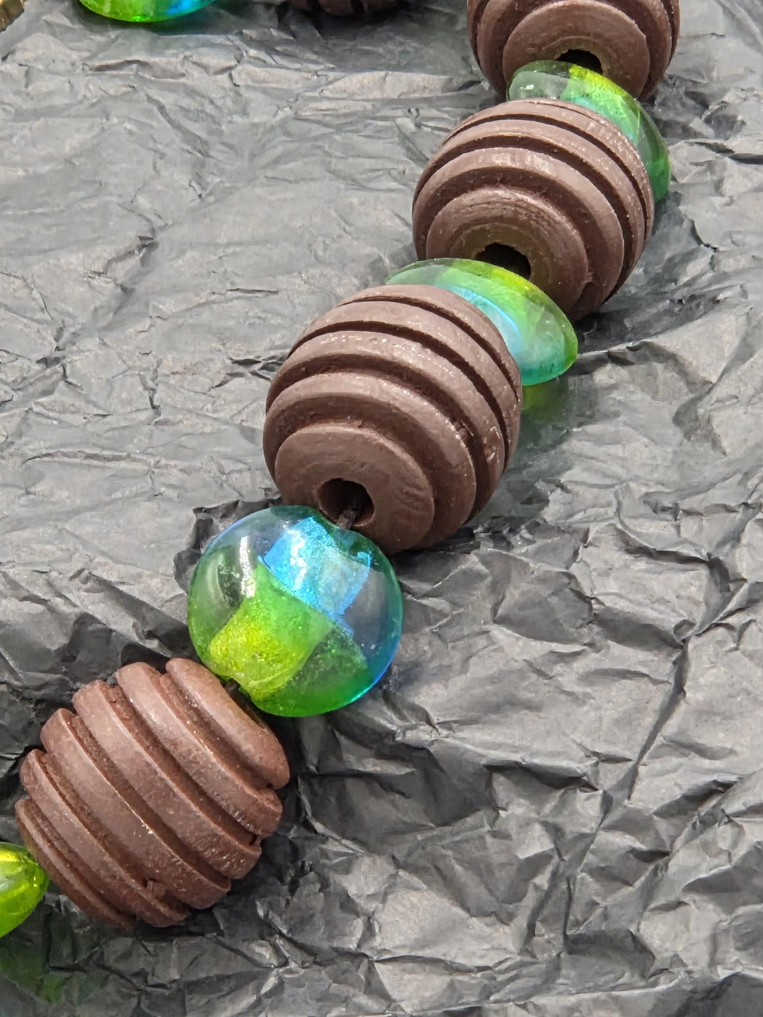 close up of Choker necklace with large ribbed brown wood beads and blue-green foil glass beads.