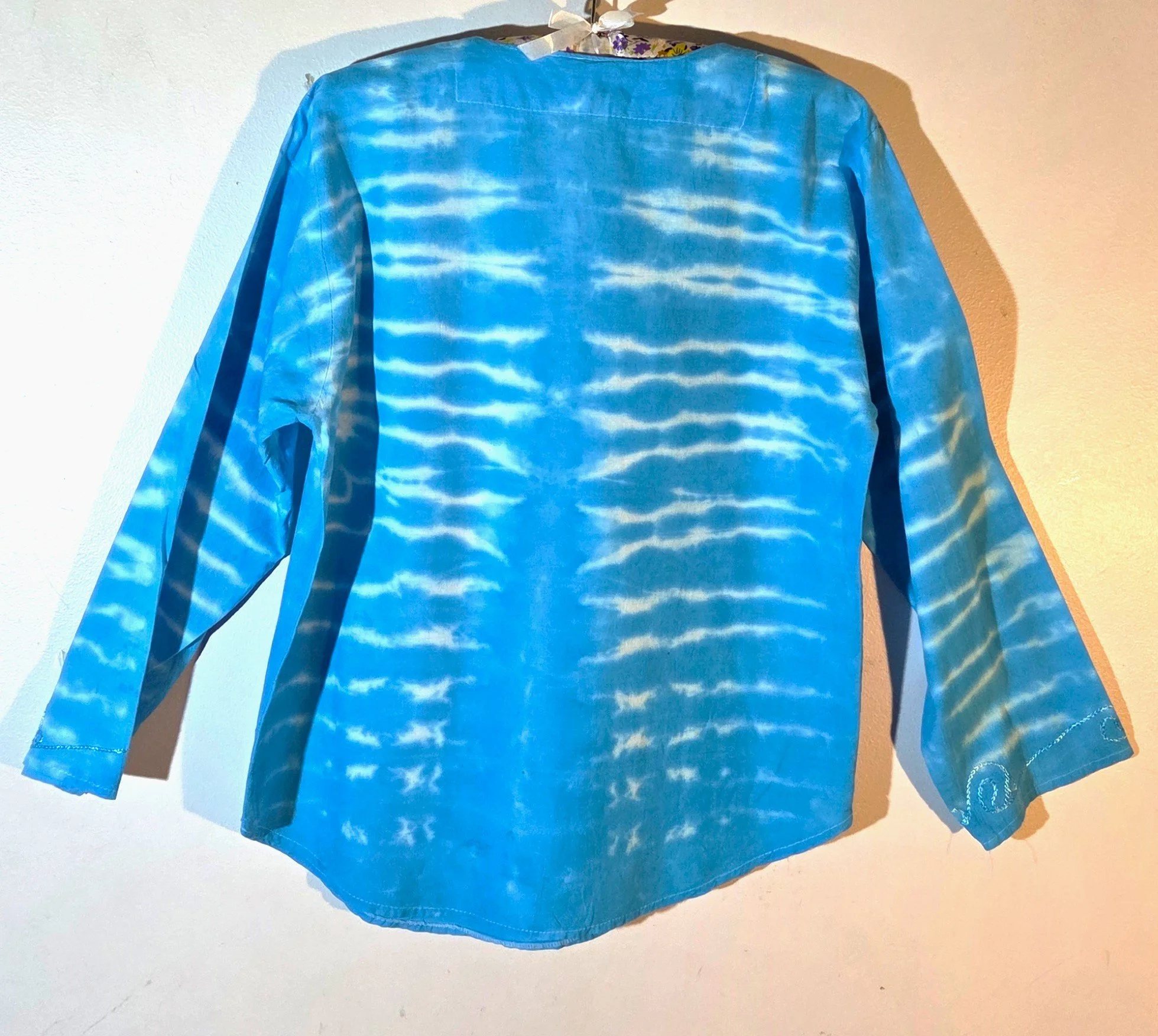 back view of A light blue cotton kaftan shirt with embroidered details, showcasing a vertical tie-dye pattern of thin, wire-like white ripple lines.