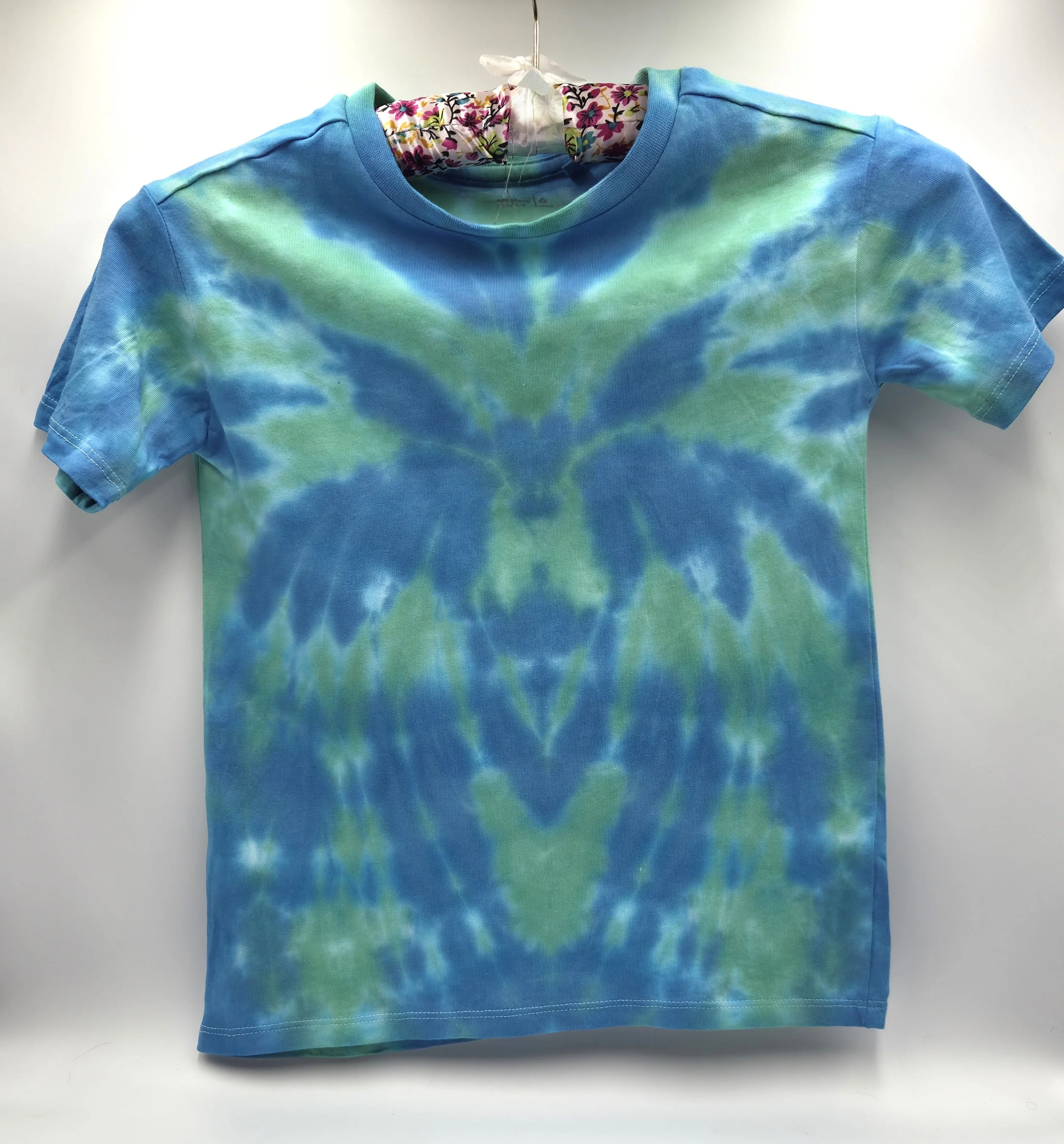 A child's light green t-shirt displaying a central sky blue tie-dye spider pattern, front view