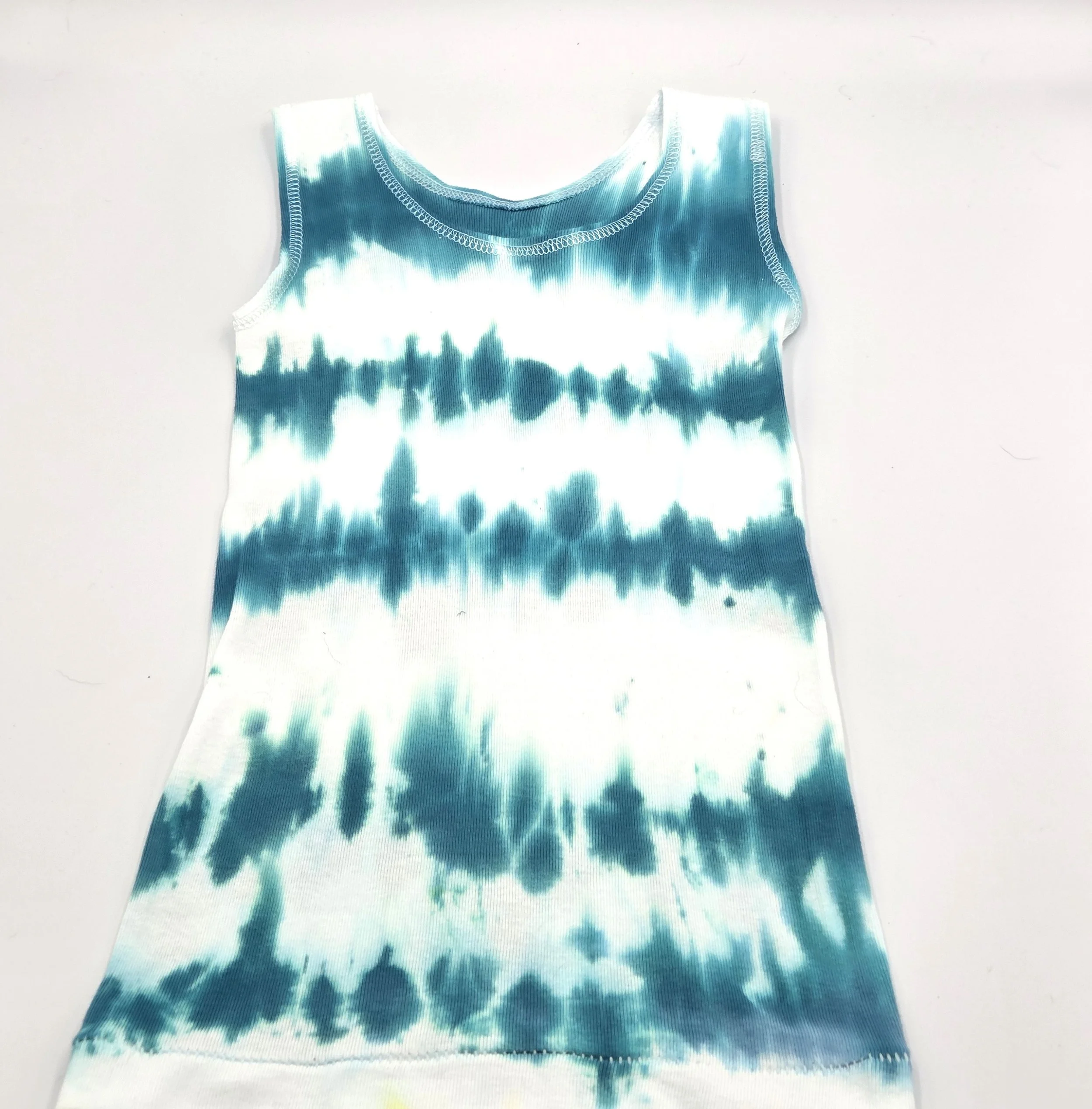 Front view of child's white singlet displaying a vertical tie-dye pattern of deep sea green wave lines.