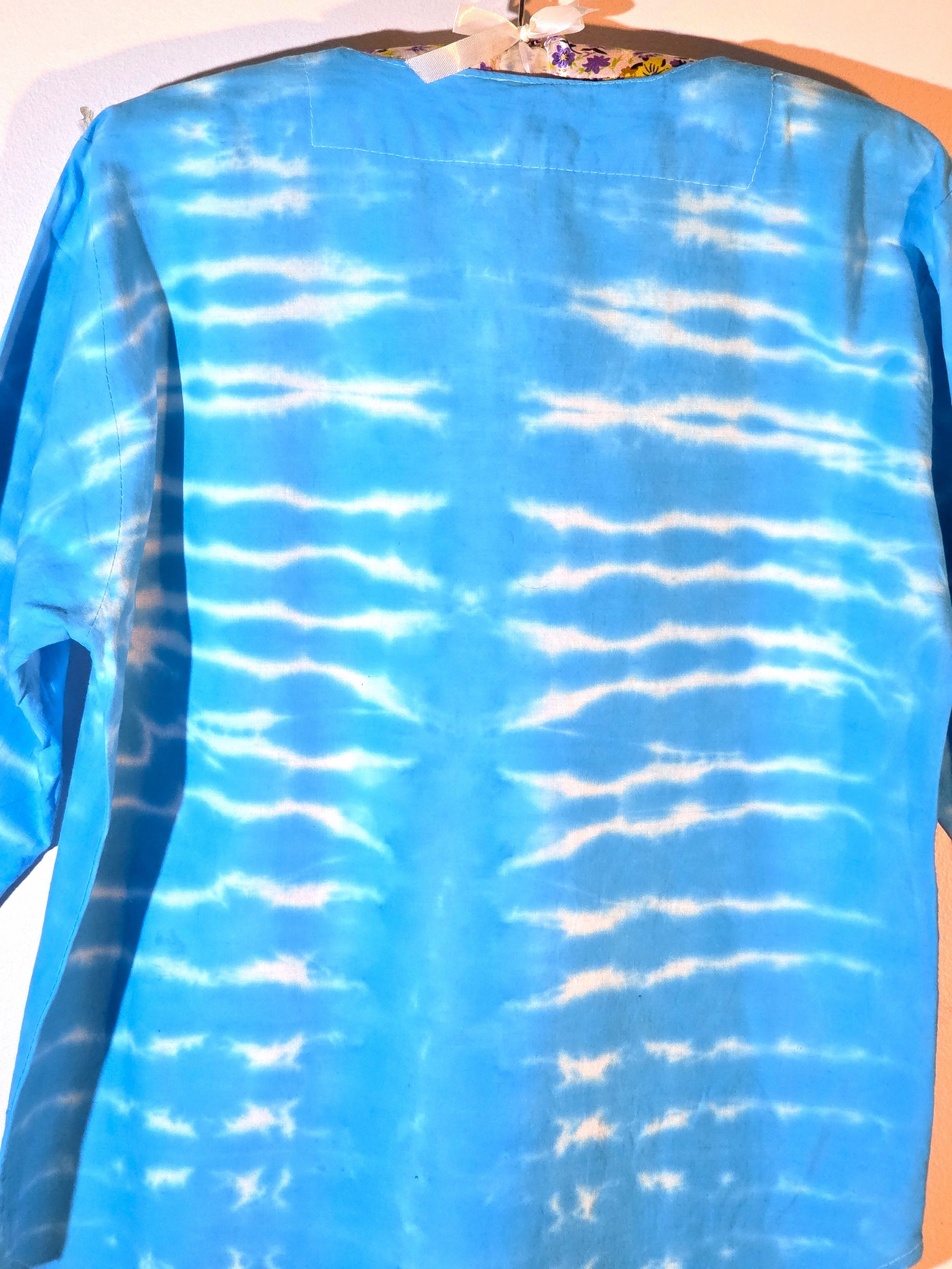close up of back view A light blue cotton kaftan shirt with embroidered details, showcasing a vertical tie-dye pattern of thin, wire-like white ripple lines.