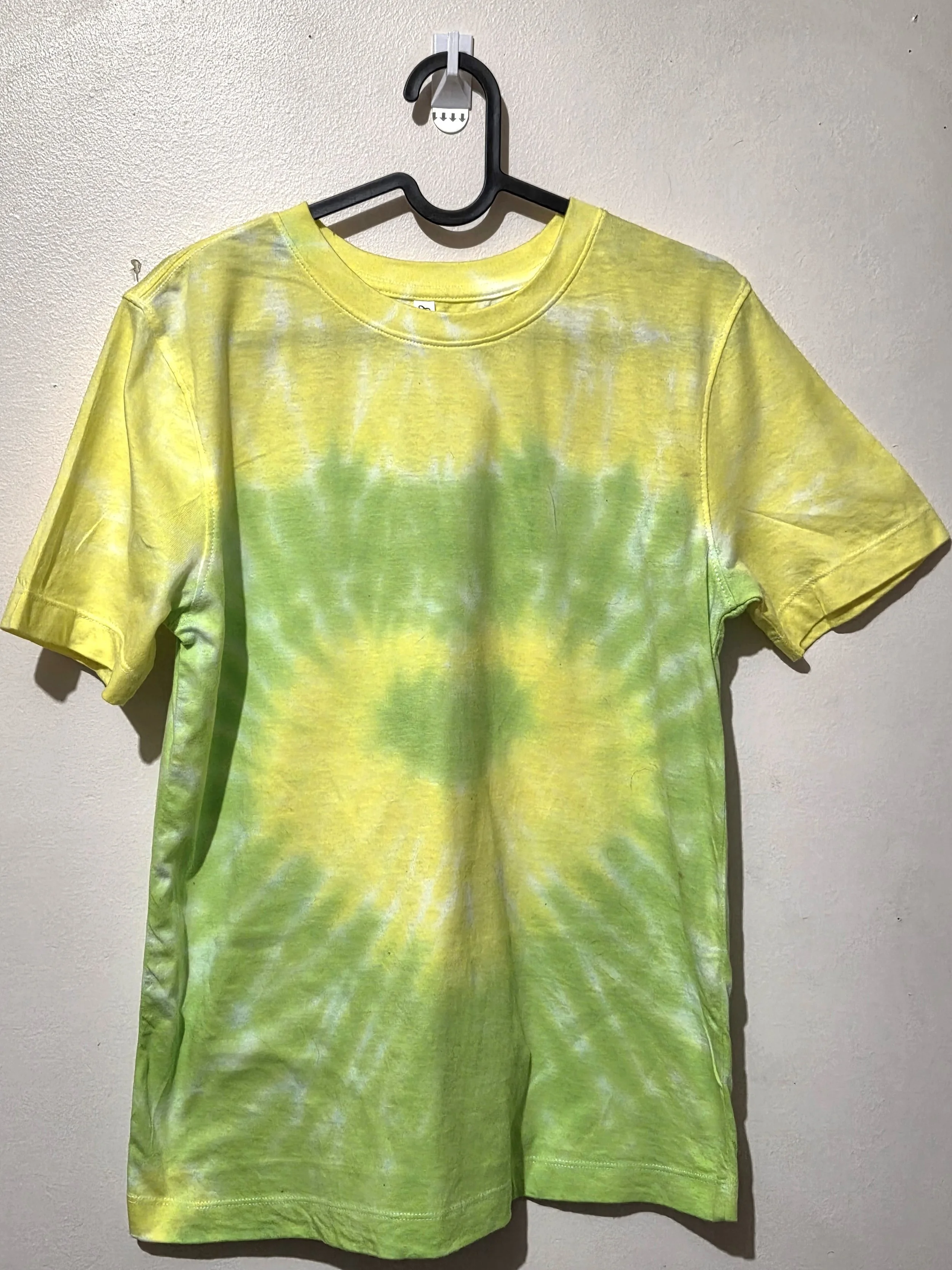 An adult size 10 women's cotton t-shirt featuring a tie-dye heart pattern in subtle pastel yellow and lime green.