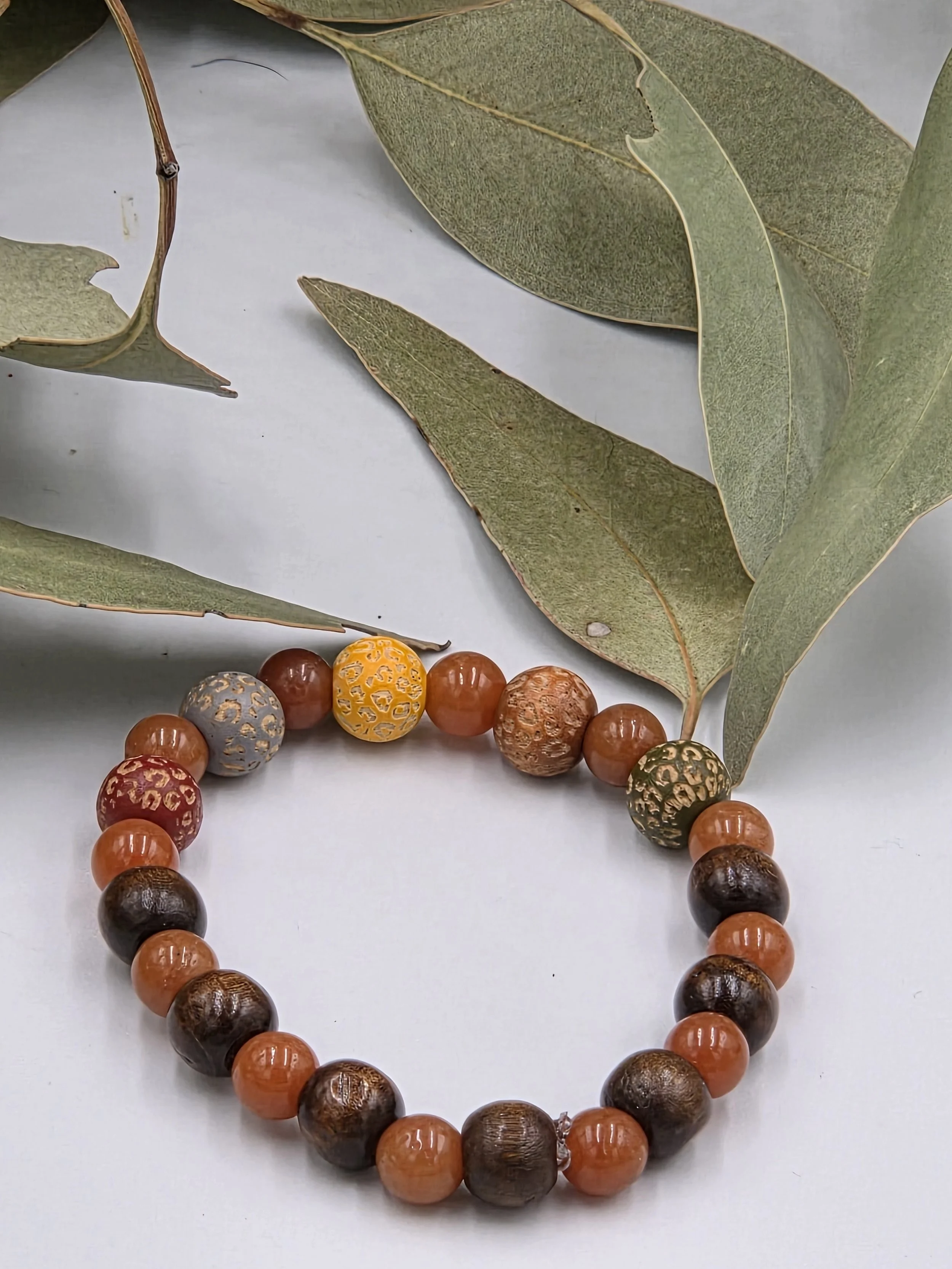 Warm red aventurine beads alternating with multi-coloured leopard print wood beads and dark brown wood beads on an elastic bracelet.