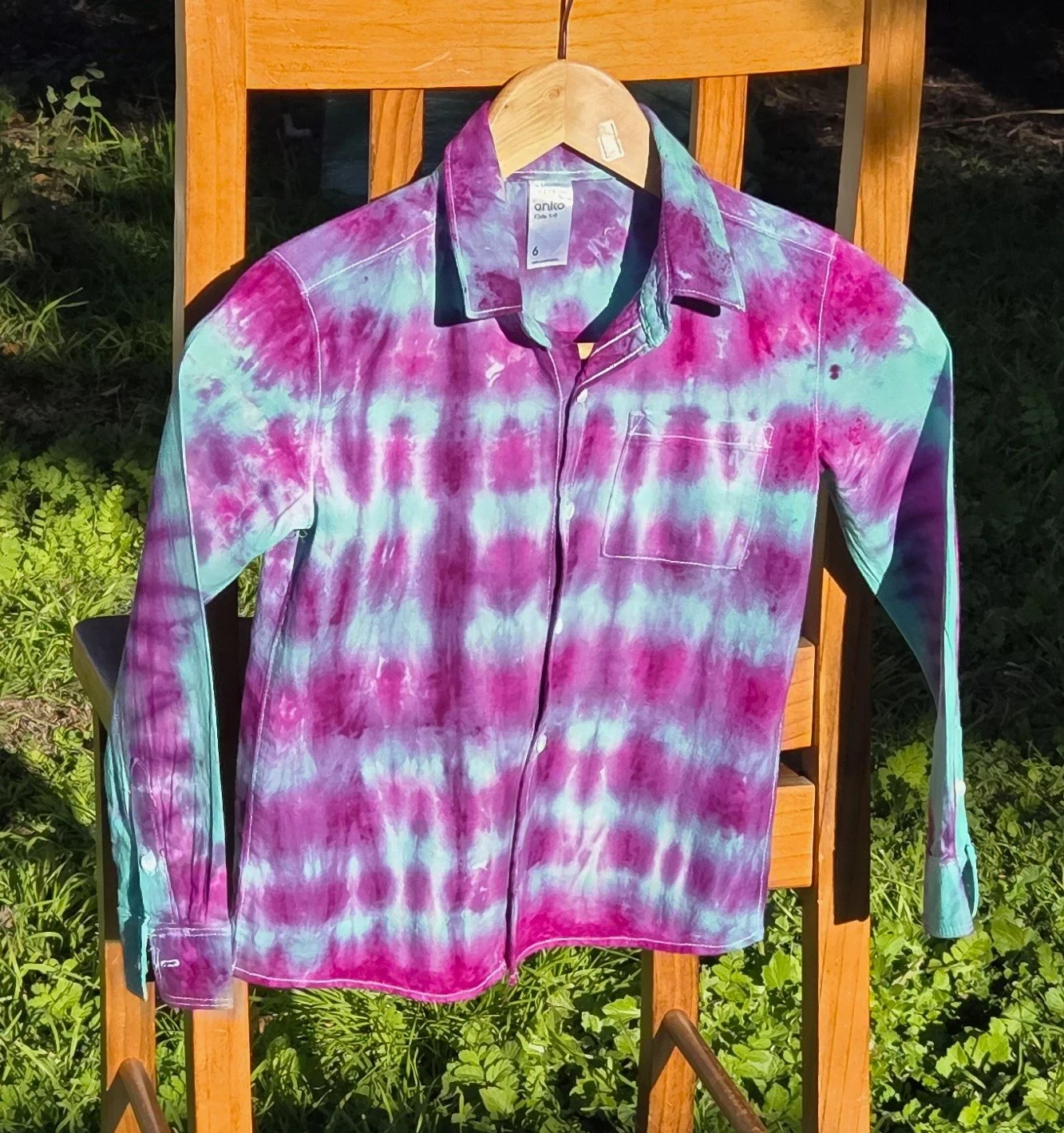 A child's size 6 long-sleeved collared shirt featuring a tie-dye pattern of consistent horizontal purple lines over a bright teal background.