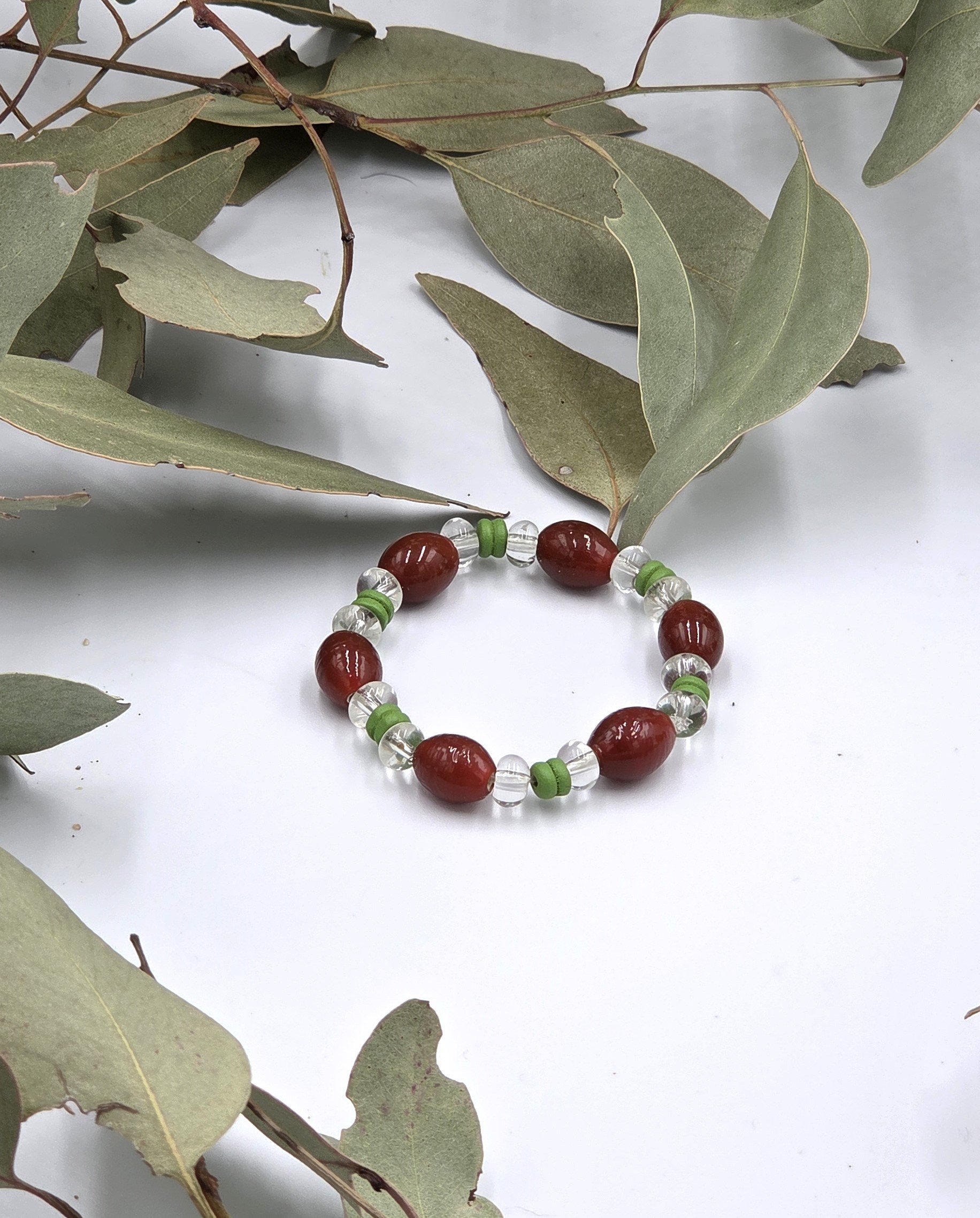 Rust red glass oval beads separated by clear glass donuts and forest green ribbed wood beads on an elastic bracelet.